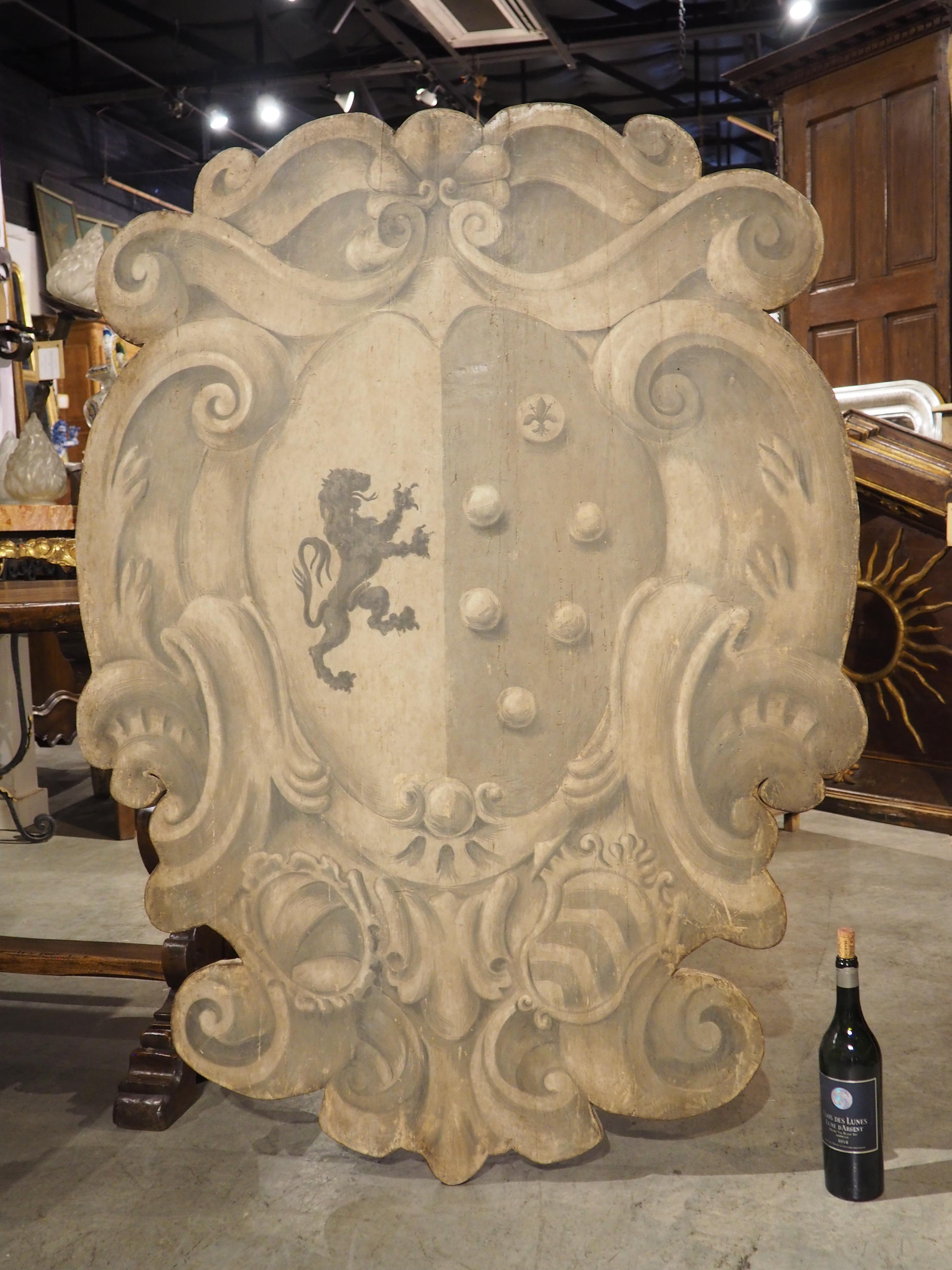 Constructed from antique salvaged wood and more recent boards, this large stemma plaque has an outward curve, reminiscent of the bend of a real shield. Hand-painted in Florence, Italy, the plaque features a grisaille-like (a painting technique that