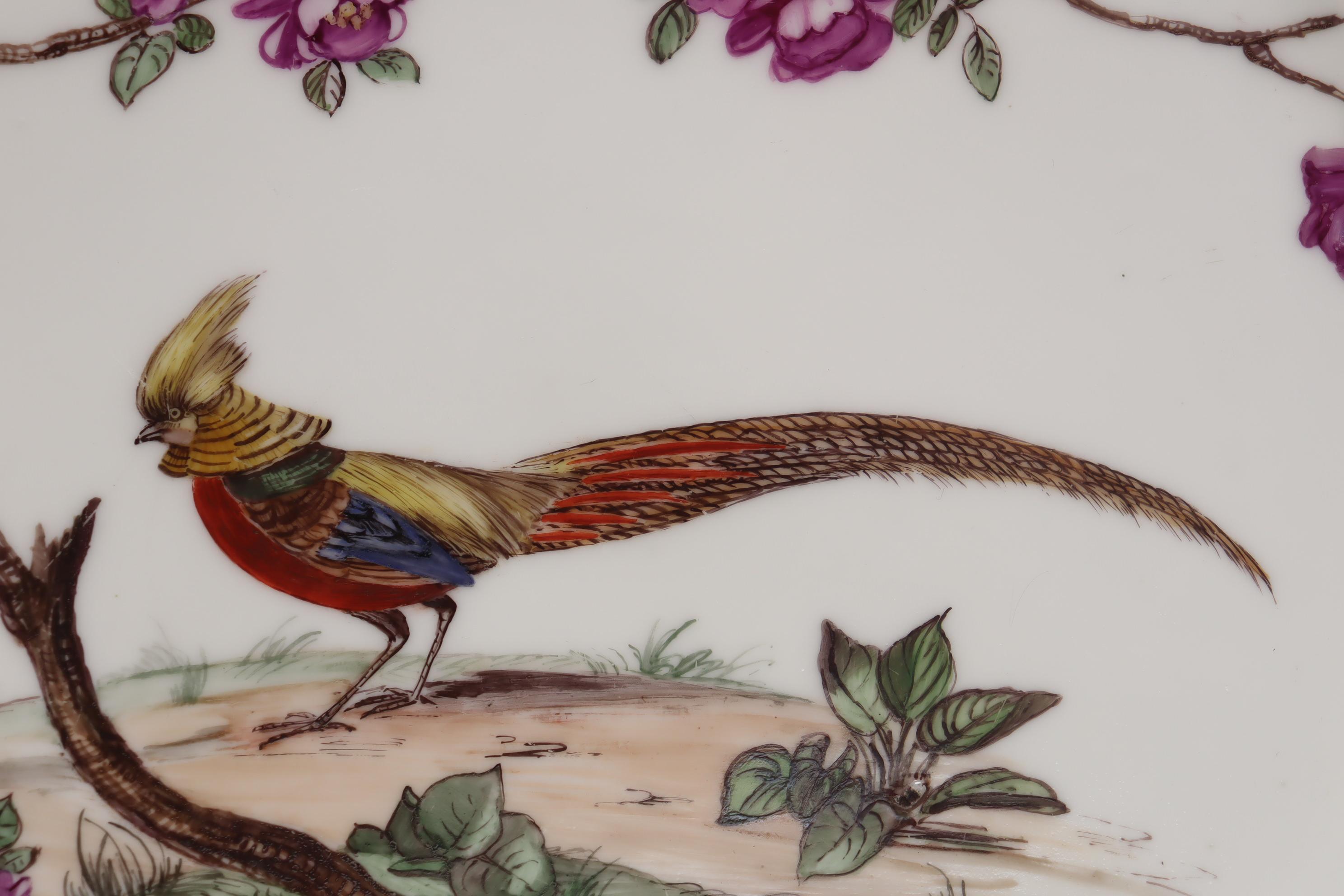 This large, very decorative hand painted French porcelain platter, or charger, features a Golden Pheasant to the centre, which is framed by a bower of purple flowers that extends to the rim in three directions, and where brightly coloured