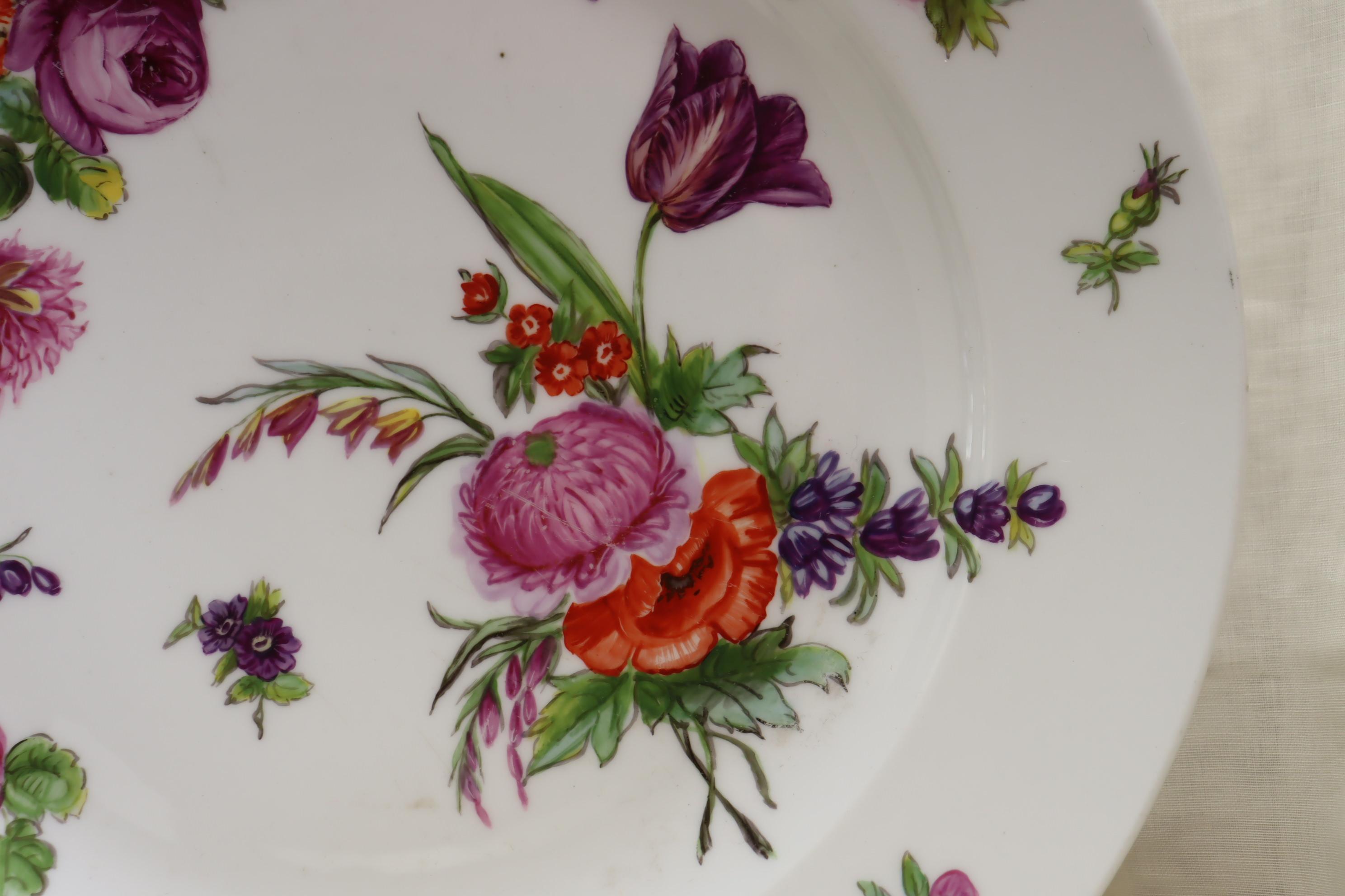 This large, very decorative French porcelain platter, or charger, is decorated with numerous scattered sprays of hand painted flowers. It could be displayed on a stand, on a wall or in the middle of a table as a decorative piece, or used as a fruit
