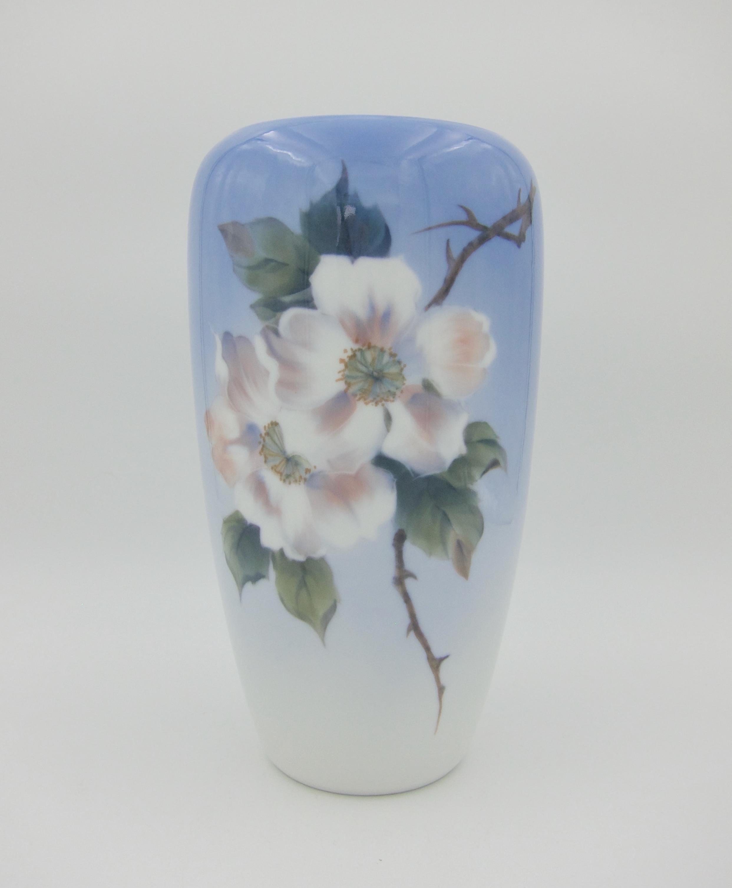A large porcelain vase hand-painted with a spray of pink and white dogwood blossoms and green leaves with a butterfly on a glossy ombre ground of pale blue from Royal Copenhagen of Denmark, date marked for 1962. The vase is in very good undamaged