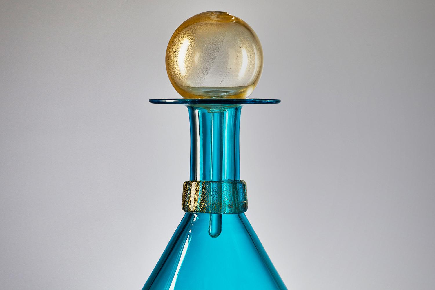 The modernist hand blown Tall Elliptical Jewel Bottle by Vetro Vero features vibrant Turquoise Blue glass and shimmering gold details. Inspired by apothecary collections and decanters of Mid-Century Modern design, the bright aquamarine carafe makes