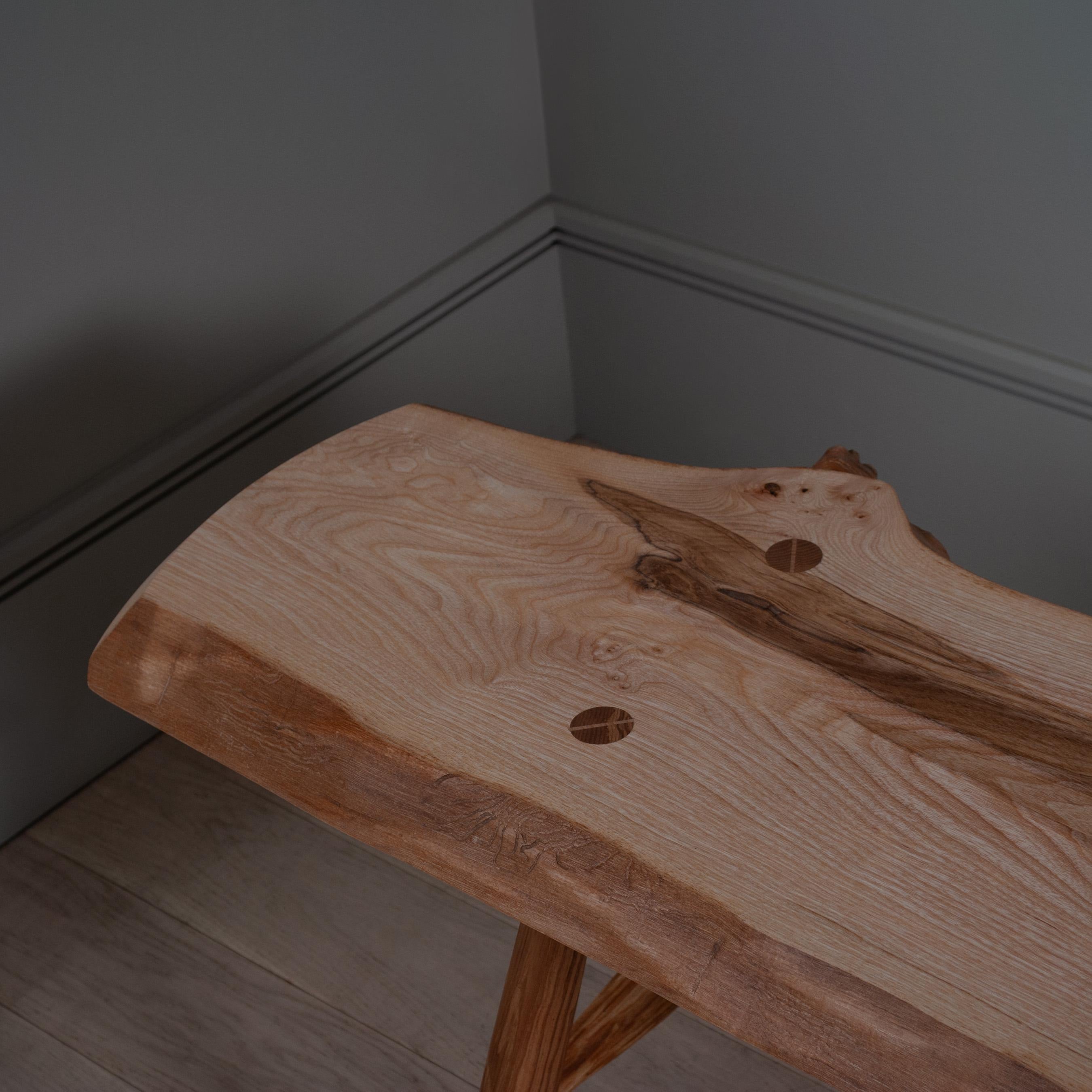 Solid olive ash contemporary bench. Handcrafted with a large live edge slab of olive ash, traditional visible wedged joints and hand-turned legs. 

This one of a kind bench is made from solid timber and the use of the traditional joinery pulls the