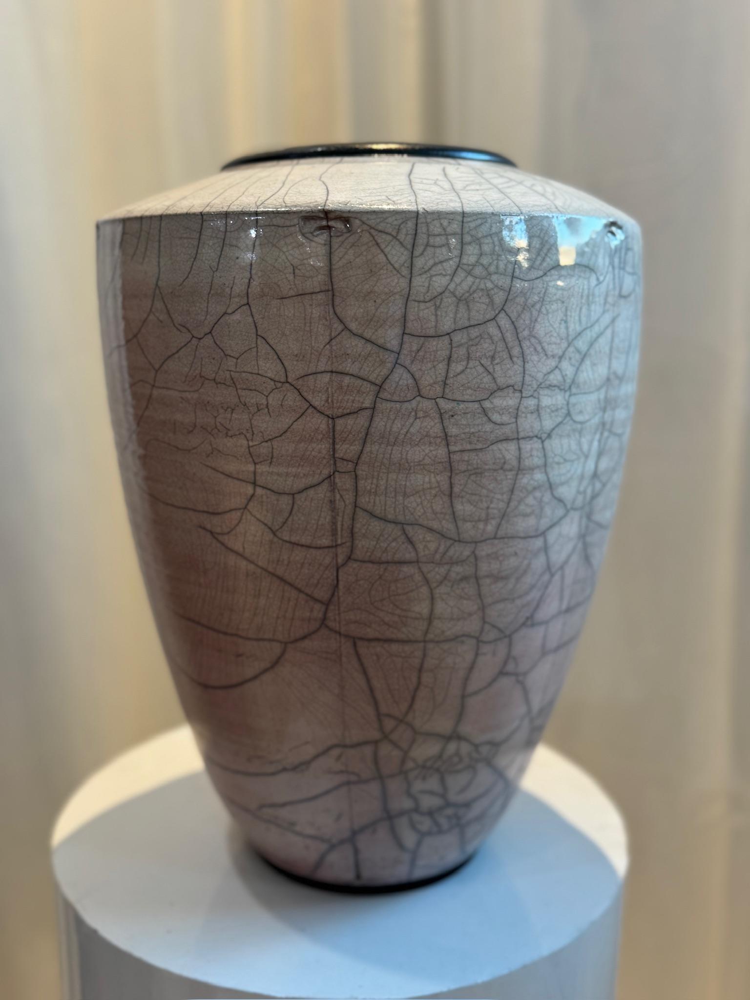 This exceptional handcrafted Raku pottery vase features a mesmerizing crackle glaze that forms an intricate web of fine black fissures across its subtly shaded surface. The vase boasts a gently rounded form with a slightly tapered base, complemented