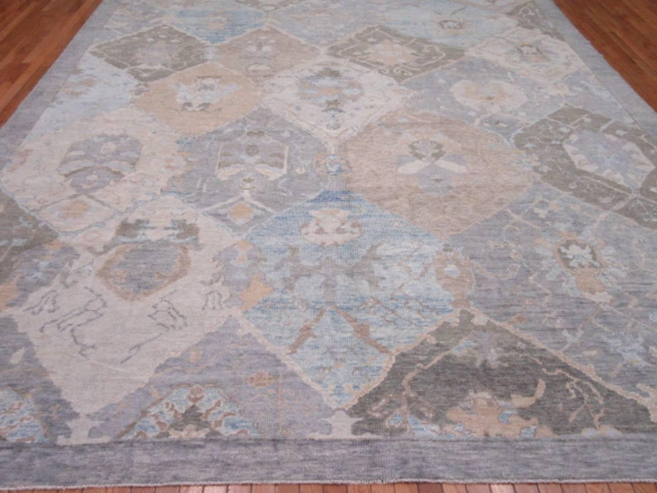 His is a large new hand-knotted wool rug from Turkey woven in the panel Oushak design. It is a well constructed rug with primary colors of ivory, grey, blue and terracotta red. Its transitional design makes it an easy rug to work with for any room