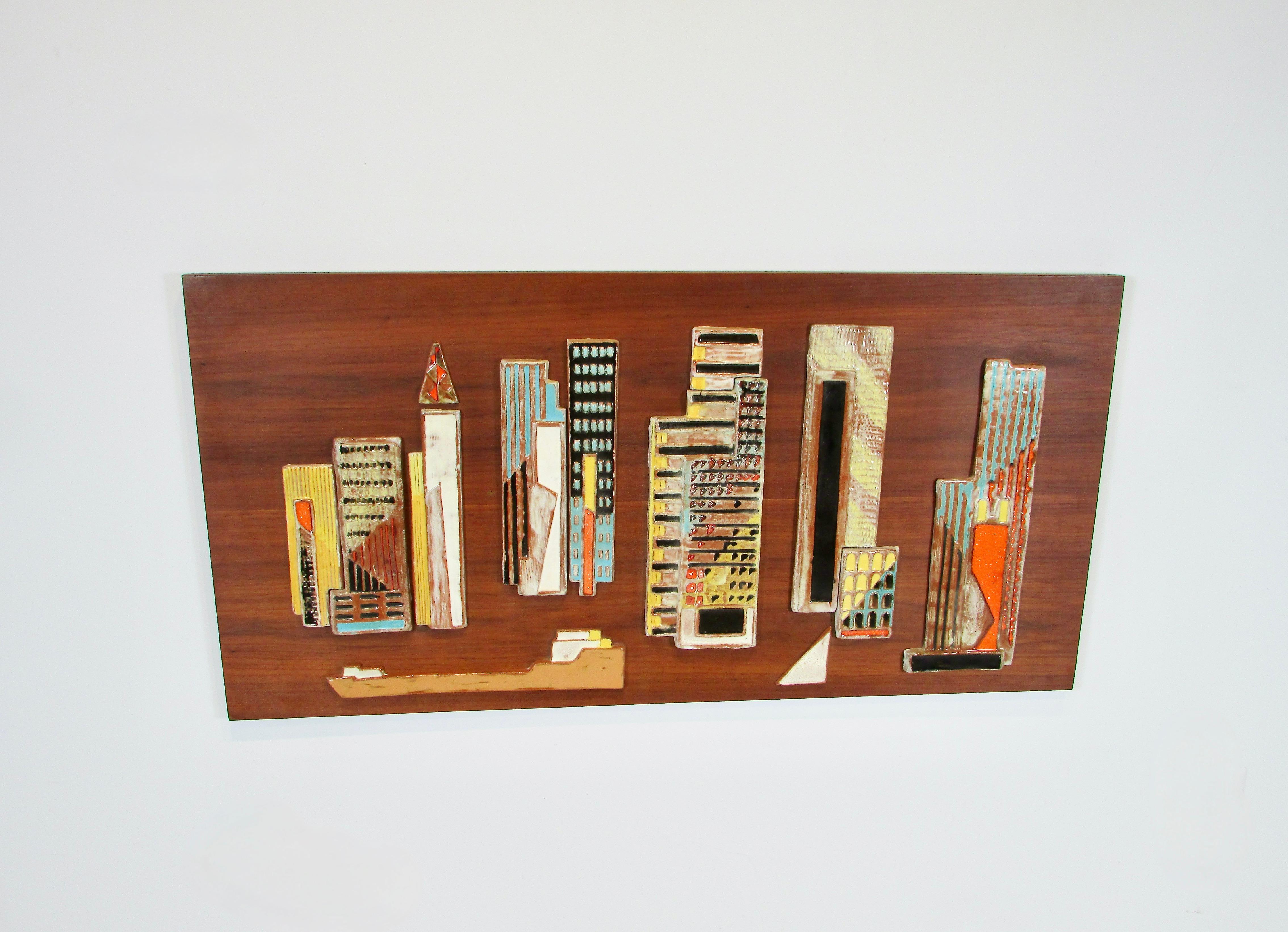 Stylized riverfront city scape of glazed and fired Terra cotta . Eight buildings with a freighter passing by . The white triangle possibly a sailboat . Glazed in vivid colors assembled by Harris G. Strong inc. Remnant of Harris Strong label on the