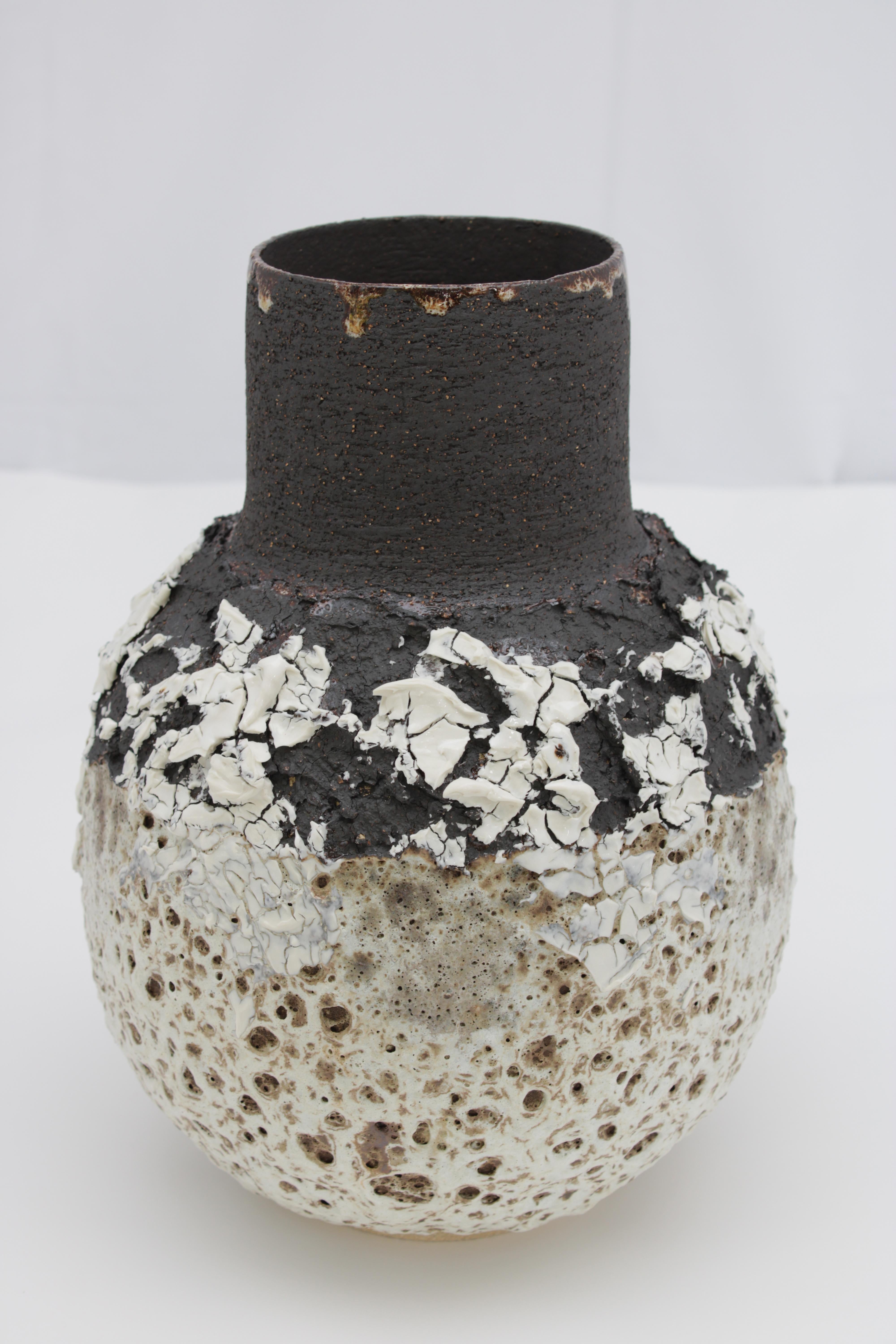 A large heavily textured volcanic vase with black, white and brown glaze and markings. Wide necked vessel with a bellied form. Made from black textured stoneware clay and porcelain.

Inspiration for the piece comes from the clay itself and the