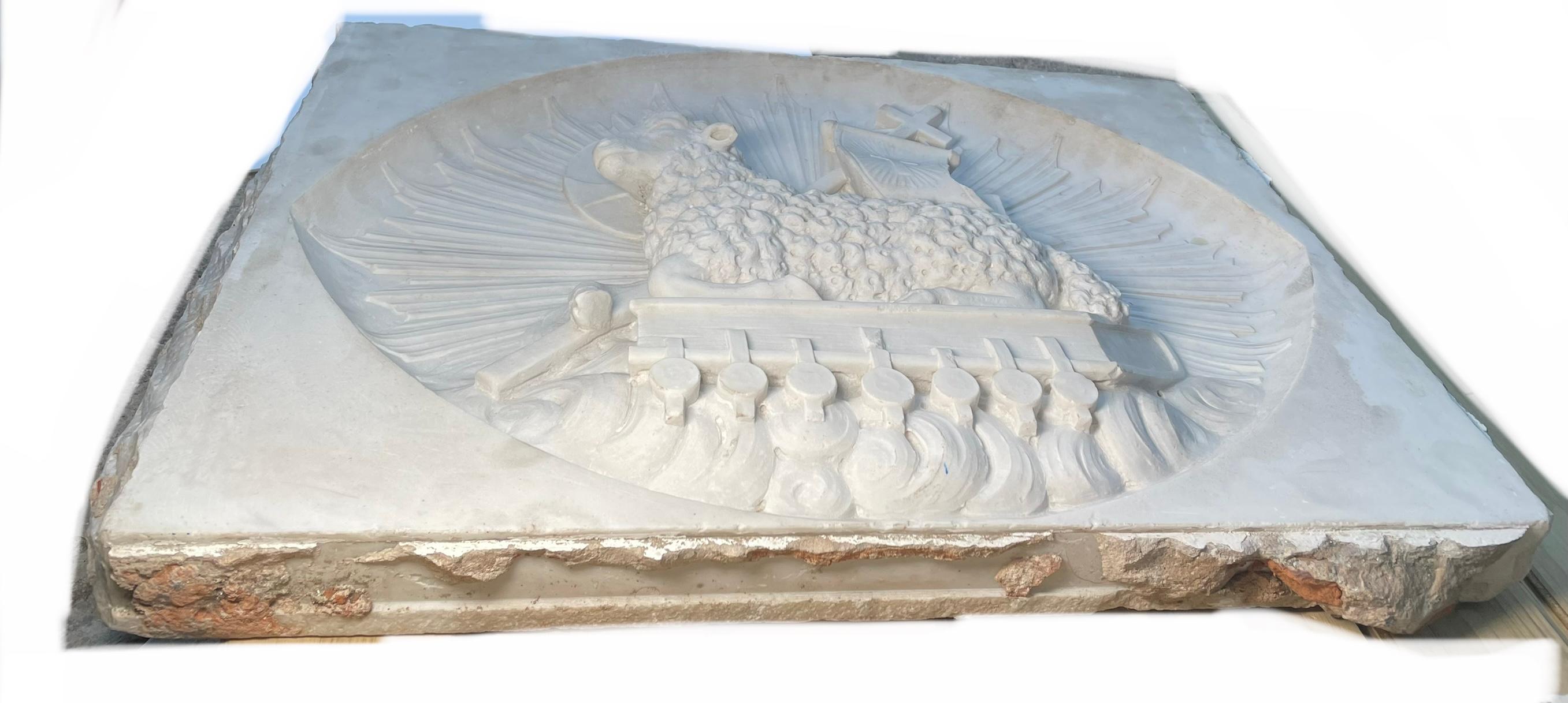 This is a large heavy rectangular shaped carved marble relief of the Agnus Dei. It depicts a lamb with curly hair seated over a Bible and bearing a cross. This one also has a banner with an engraved cross. A halo with a cross is around the lamb