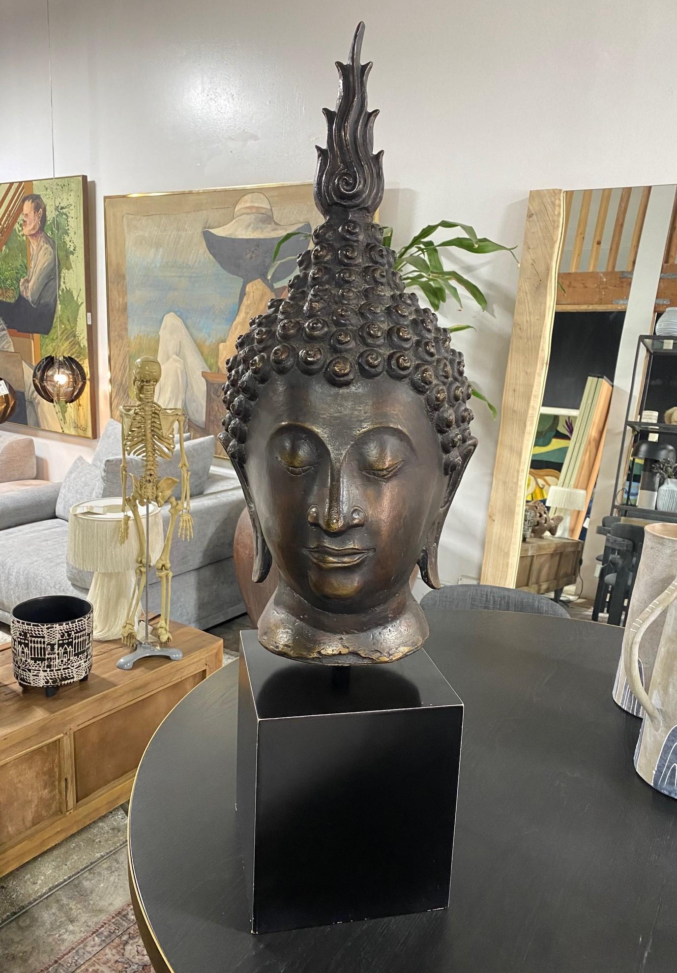 This is truly a spectacular work A beautifully sculptured Buddha head (the features and finial suggest that it is Thai/ Siam) on a custom display stand. The Buddha's eyes are semi-closed in serene meditation. The work has a nice almost bronze-like