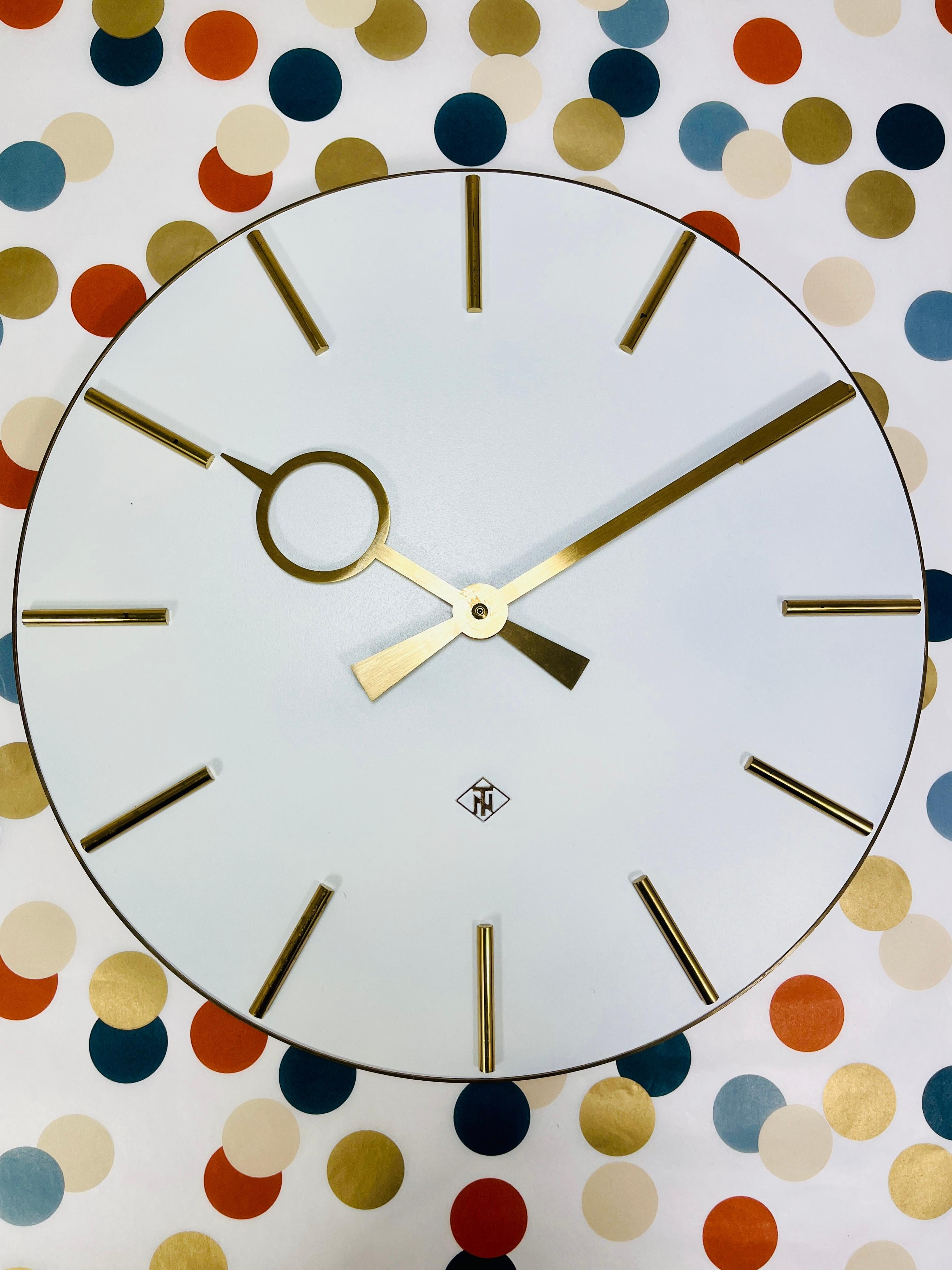 A beautiful round modernist wall clock from the 1950s, made in Germany. It features a white clock face encircled by a brass frame with sleek brass indices and elegant brass hands reminiscent of Heinrich Möller. The clock has a diameter of 16 inches
