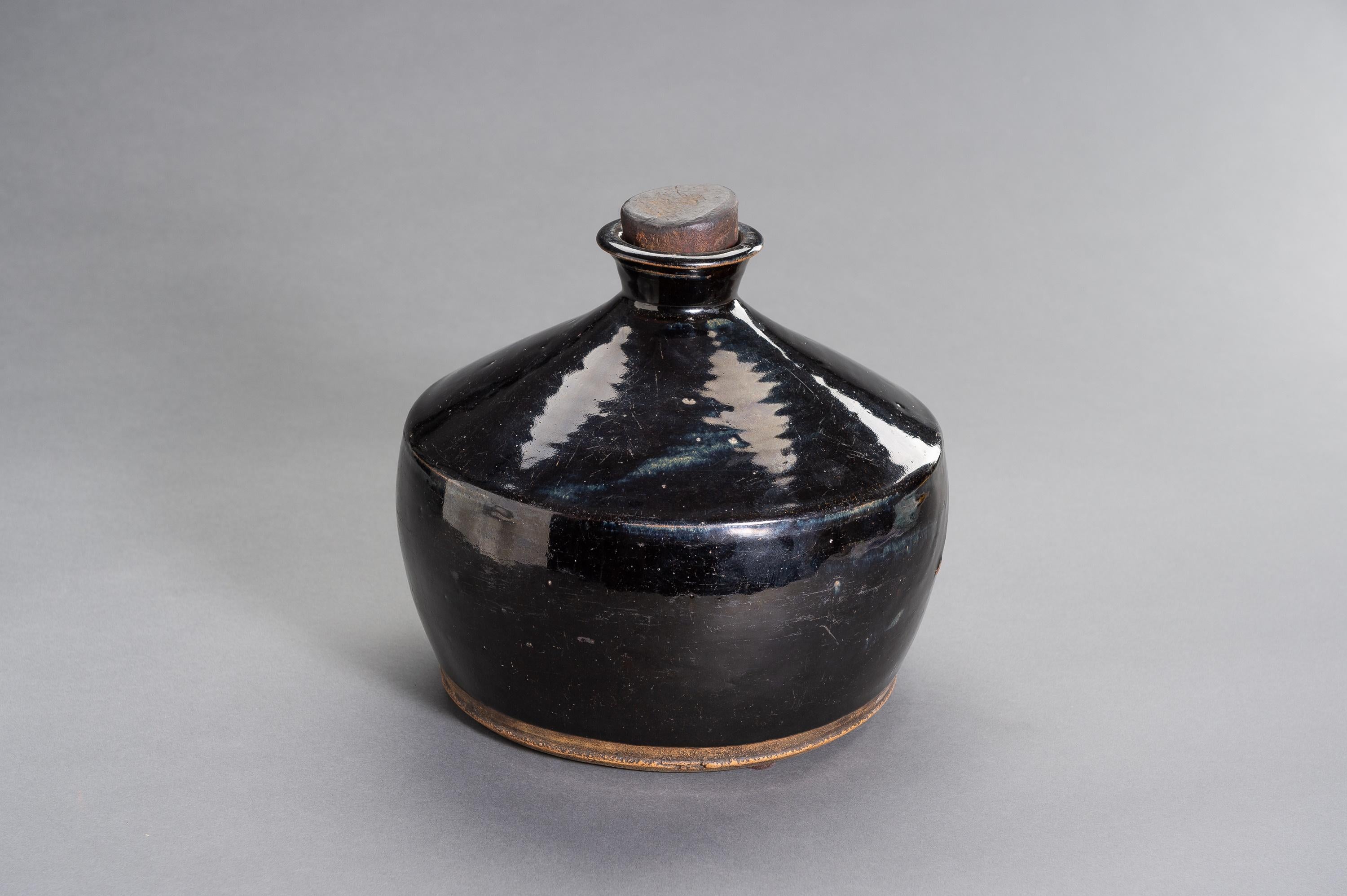 Grande bouteille henan à glaçure noire, Chinois, dynastie des Song, de 960 à 1279 ADS

Le corps globulaire comprimé s'élevant d'un pied court et large à un épaulement conique avec un col cintré et une lèvre éversée, recouvert d'une glaçure noire