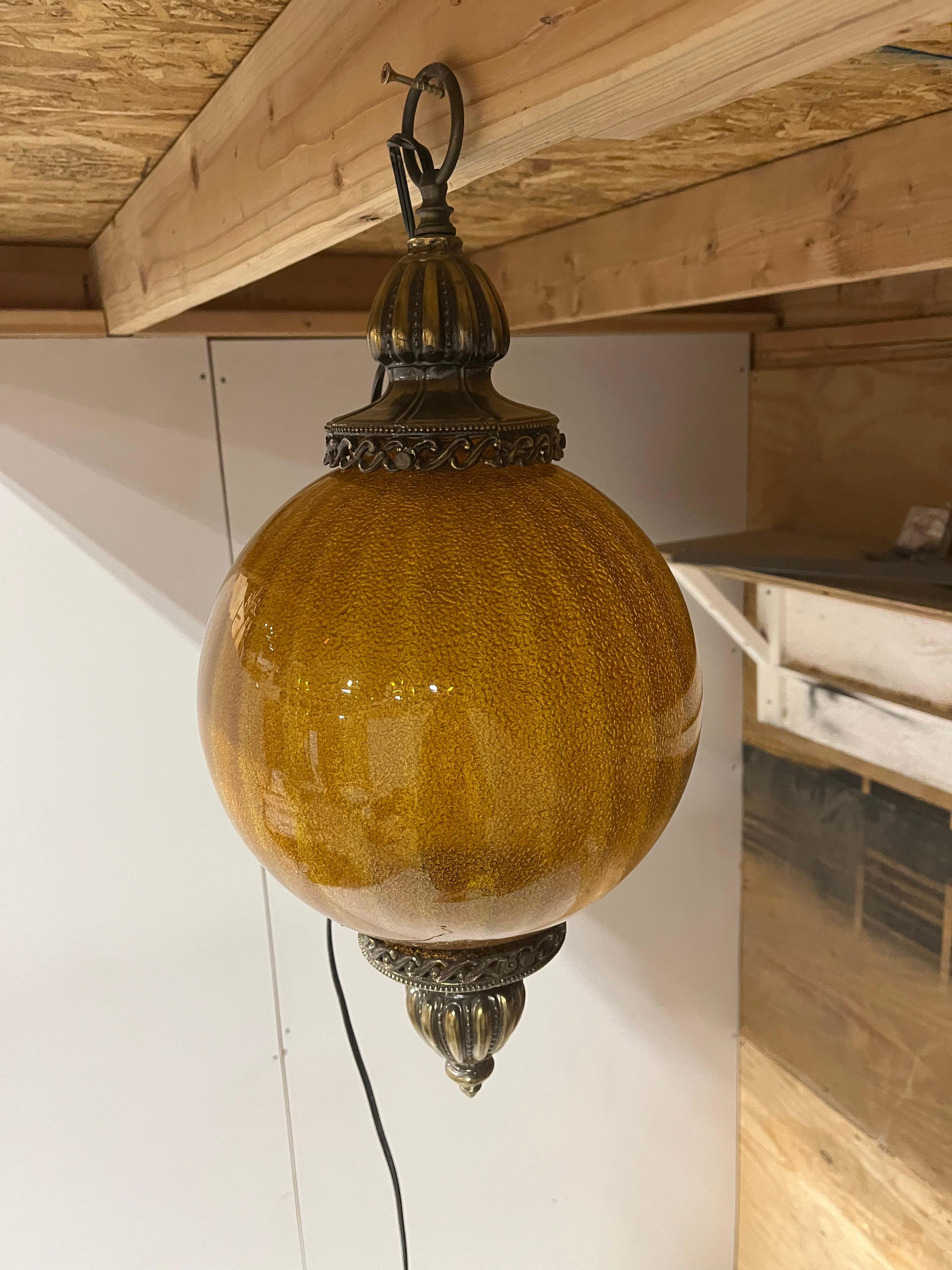 This eye-catching lighting fixture typically features a substantial amber-colored glass globe or shade, often adorned with intricate patterns, faceted textures, or ornate etchings that cast warm, golden hues throughout a room. Encased in polished