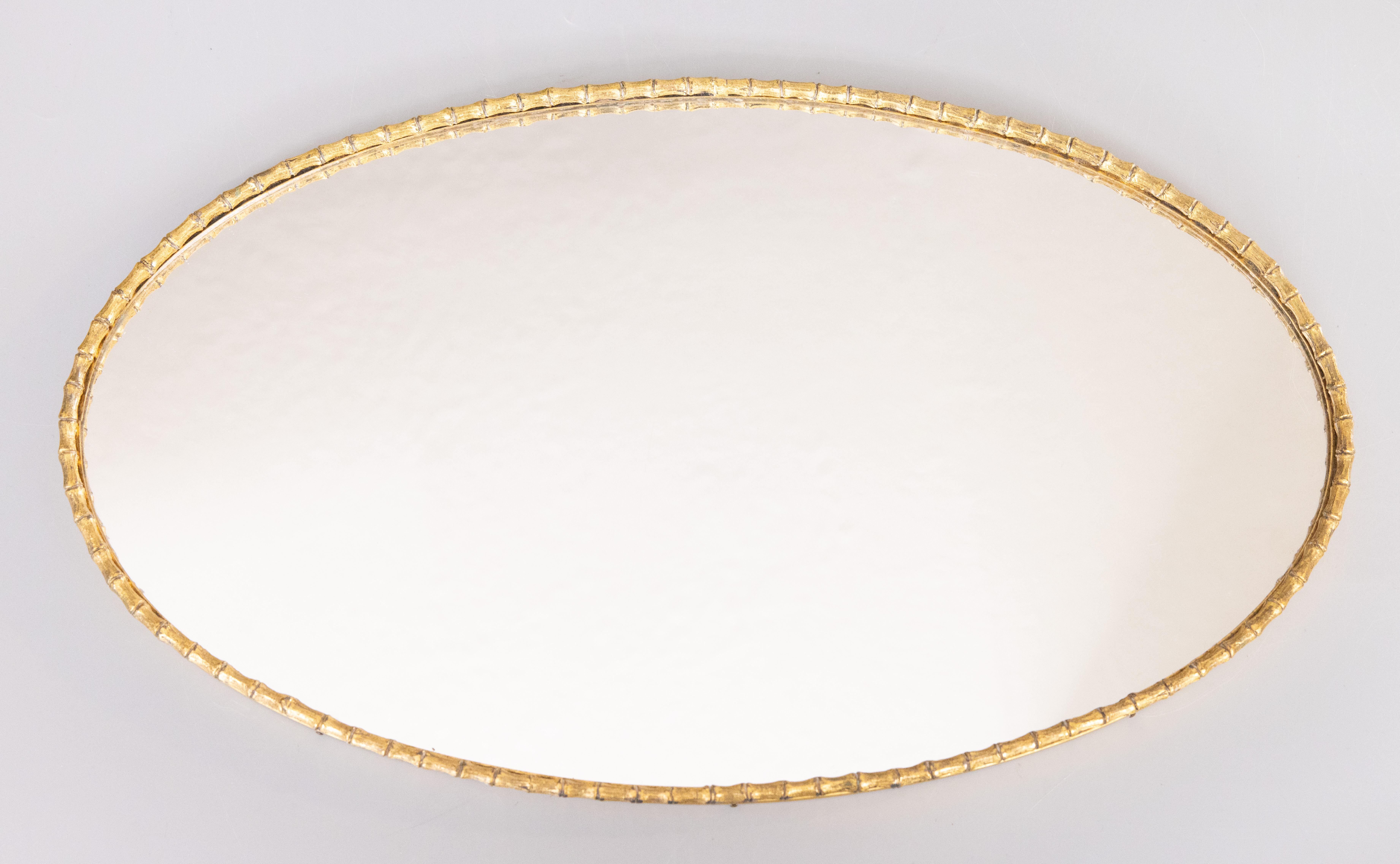 A stunning large vintage Mid-20th Century Hollywood Regency faux bamboo gold ormolu oval mirror vanity dresser or barware tray. This stylish mirror is surrounded by a gilt faux bamboo design and floral ormolu details, perfect on a vanity with