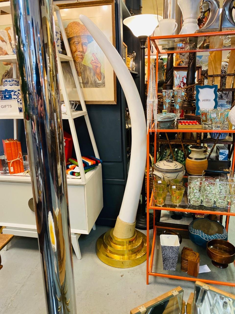 Monumental vintage Hollywood Regency pair of faux elephant tusks mounted onto a brass plated 3-tier metal base. The tusks are sculpted out of ceramic resin with a beautiful white gloss finish. Majestic in size and style. Complements midcentury,