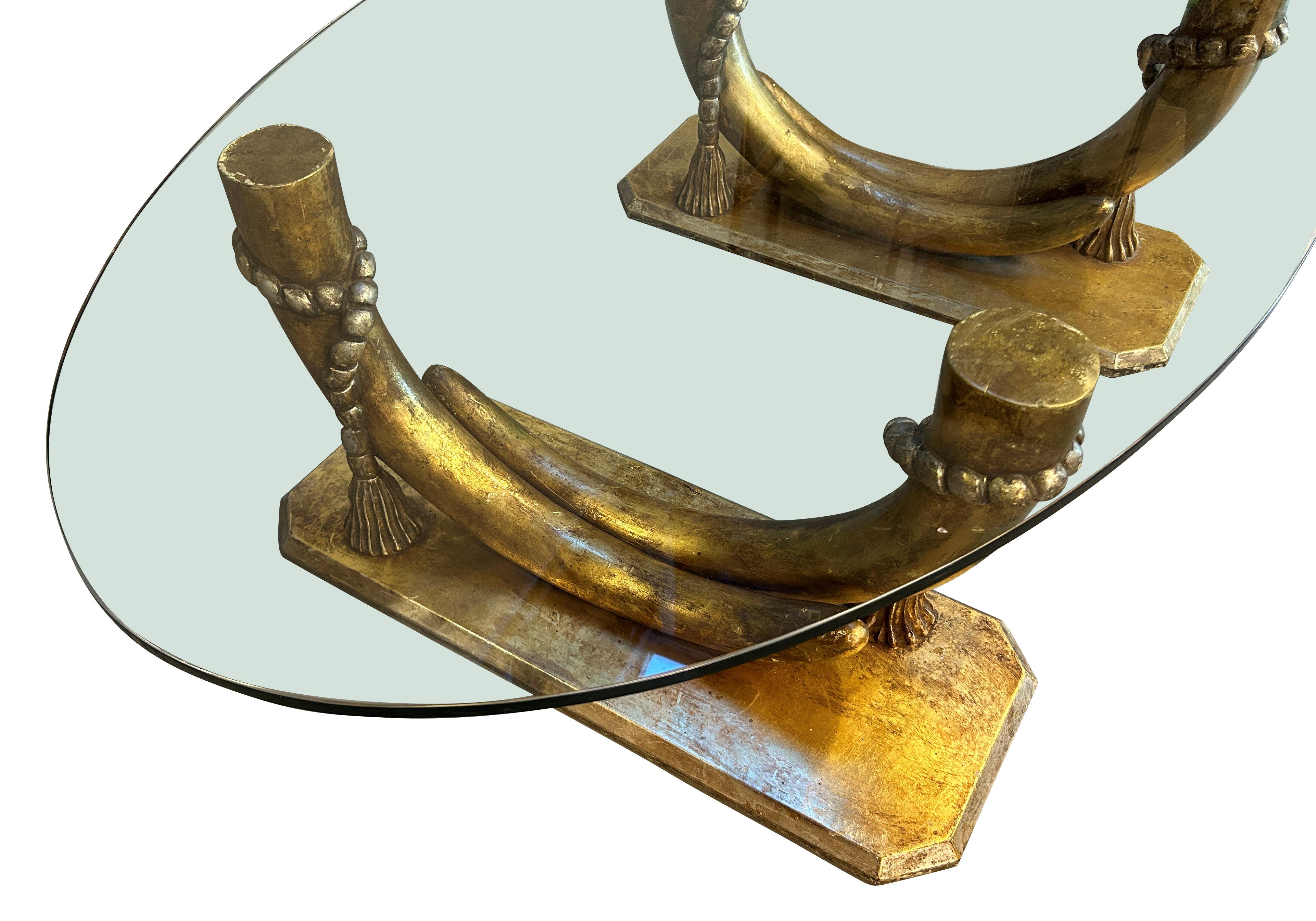 Grande table d'appoint italienne, Hollywood Regency, avec une base en bois sculpté représentant des défenses en argent et en or, supportant un grand plateau ovale en verre.