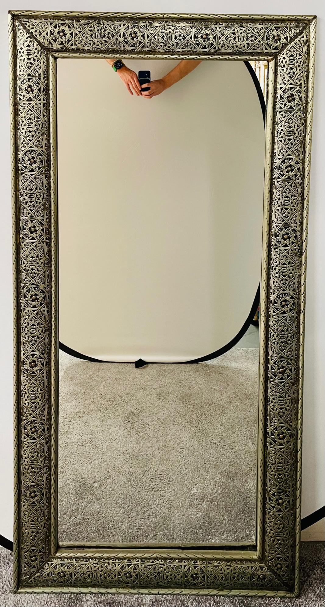 An elegant large Hollywood Regency style wall mirror finely handmade Moroccan filigree motif in a silvered metal tone. The mirror features a brass inlay and floral design and can be displayed both on the wall or on the floor. This one of a kind