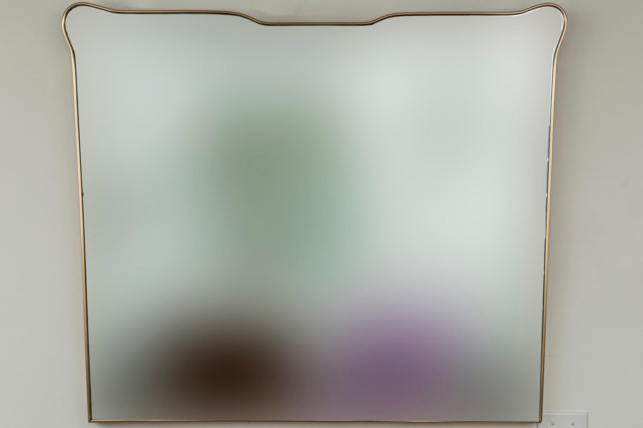 Un grand miroir unique, légèrement effilé, en forme de bouclier angulaire avec une couronne évasée.    Noter la taille merveilleuse  pour un placement horizontal.
Le laiton non laqué a été récemment poli et s'oxydera bientôt pour devenir plus