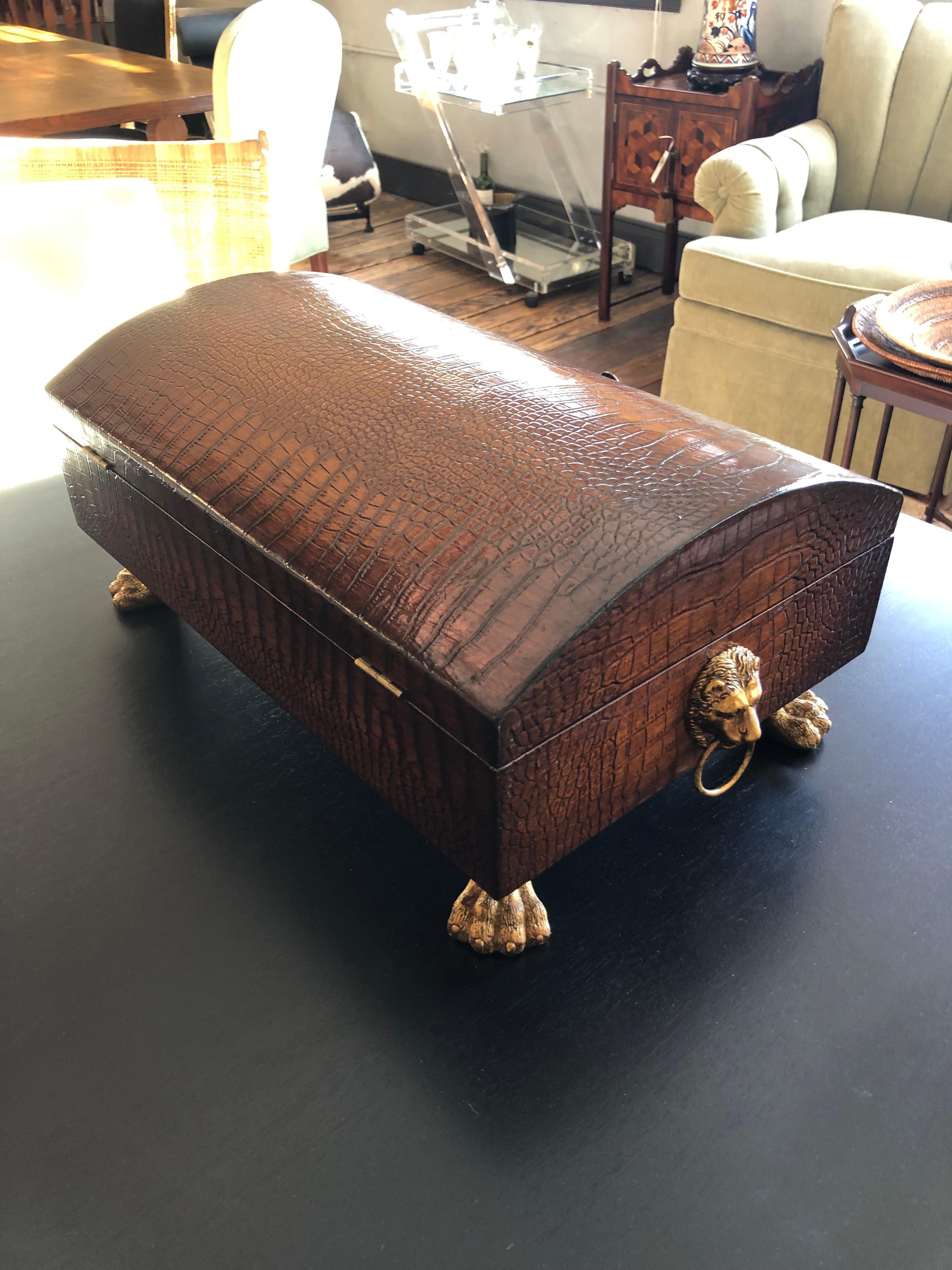 Stunning large carved wood decorative box having the appearance of rich crocodile.  There are brass lion head handles on each side, a round knob for opening, and handsome paw feet.