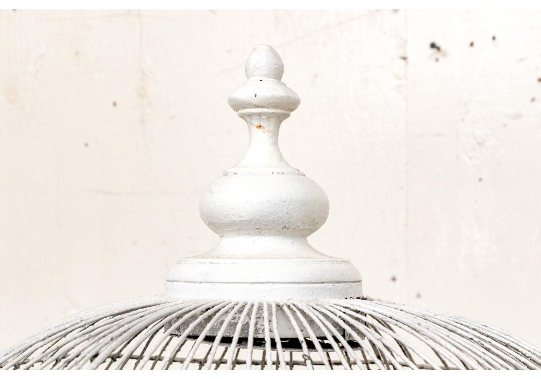 An impressive vintage iron and wood white paint decorated multi-dome birdcage with compatible iron base. The birdcage with three functional doors, wood finials, wood trim and wire construction. The metal cleaning tray is missing and green styrofoam