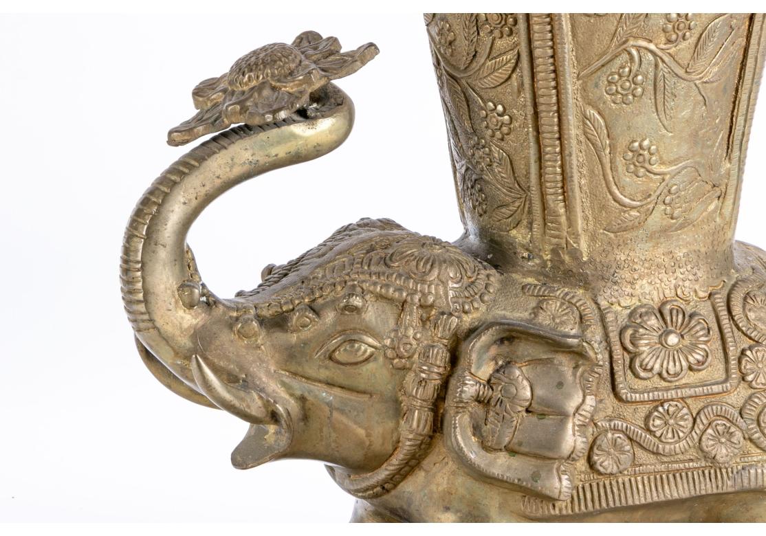 Un support de canne/parapluie indien décoré de façon complexe, avec un bon poids et un style exotique remarquable. Un éléphant agenouillé, orné de décorations, soutient une fleur dans sa trompe levée. Le récipient ci-dessus présente des panneaux