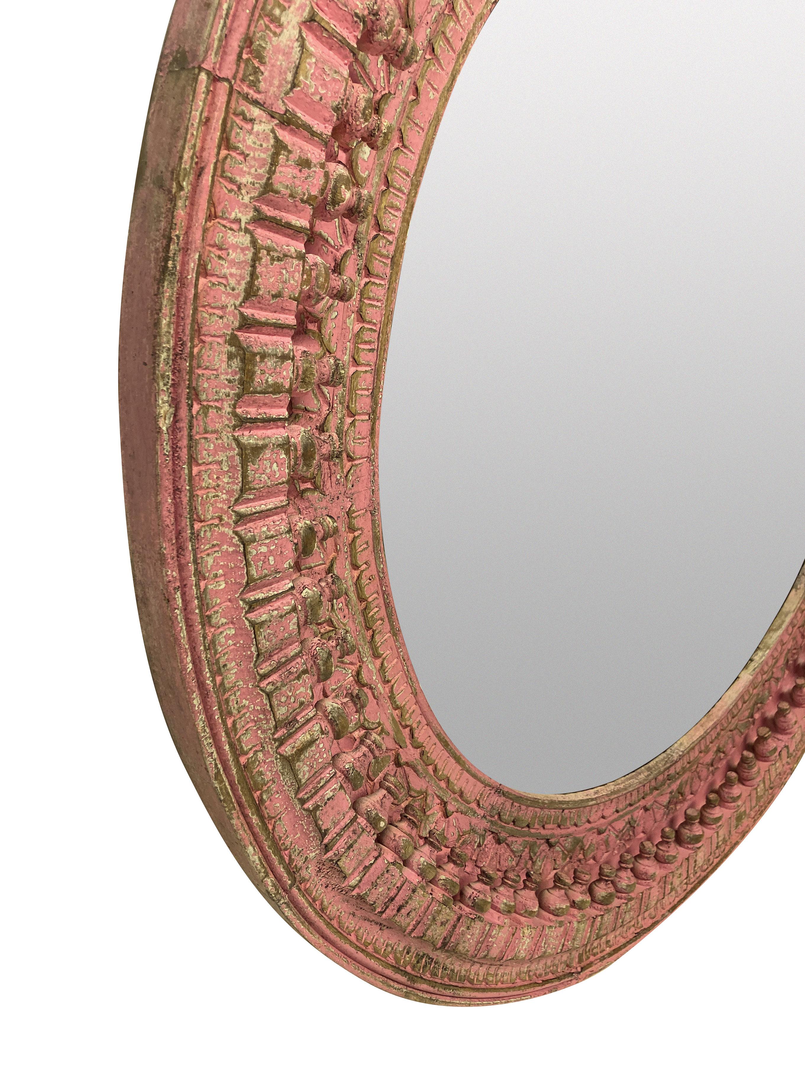 A large Indian carved hardwood circular mirror in delicate pink paints.