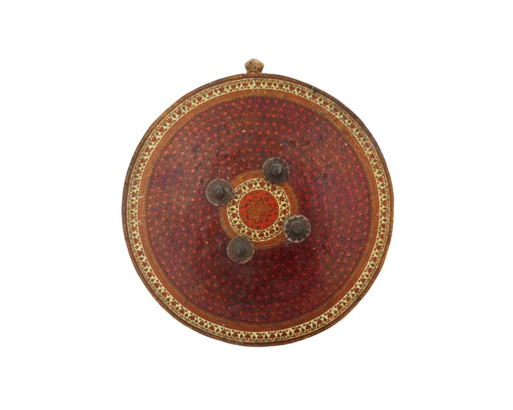 A large Indian papier mache ceremonial Dhal shield. The round, slightly curved Dhal shield with four metal bosses is richly decorated with a rhythmic, hand painted pattern in red and yellow. The inside has fabric holders and a square knuckle rest