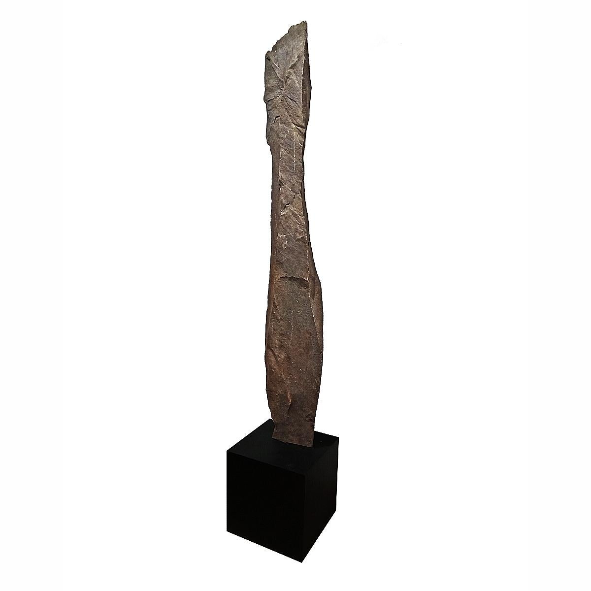A tall stone sculpture hand-carved in Indonesia, mounted on a black metal cube stand. Narrow slate. The sculpture itself is 10