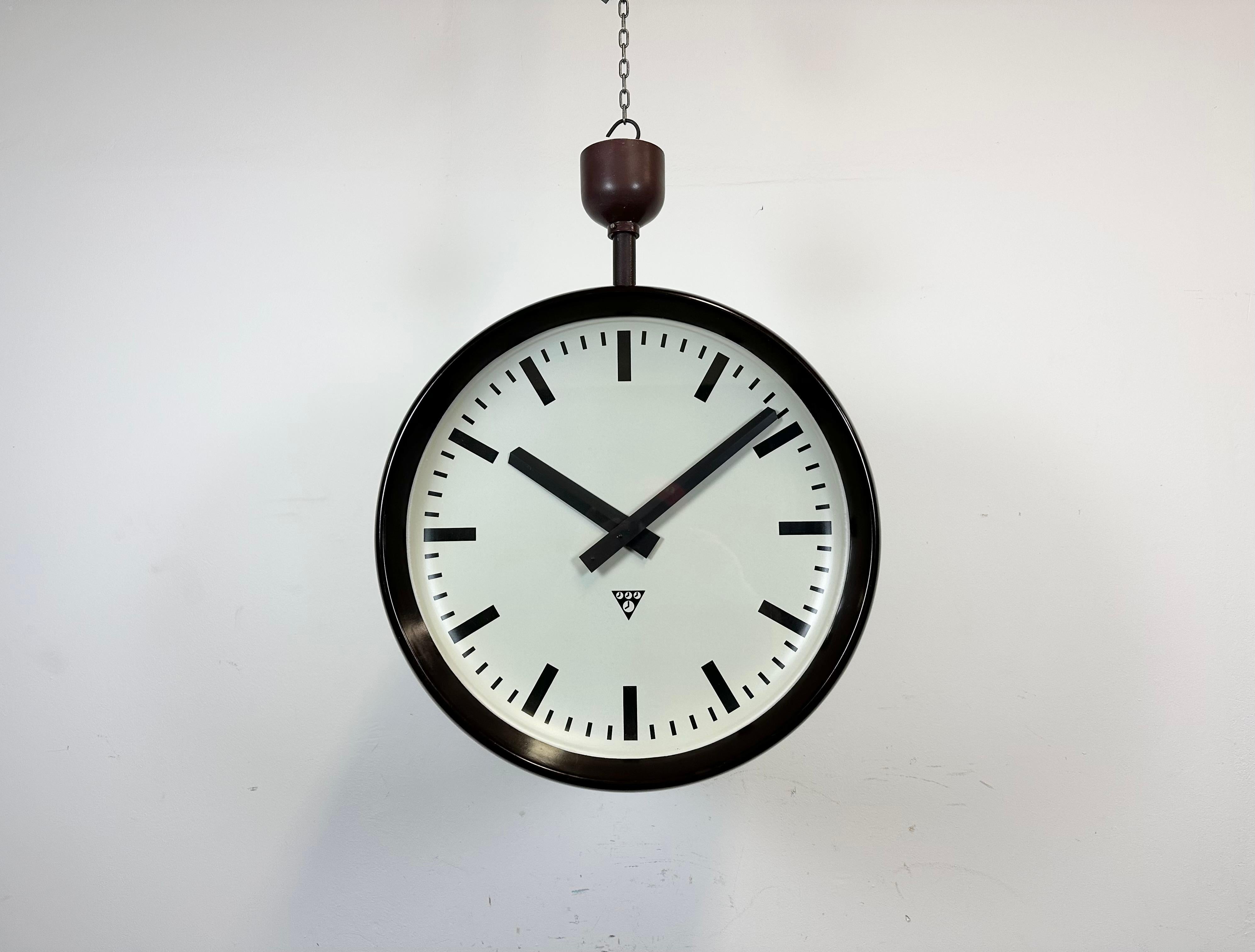 Cette grande horloge d'usine à double face a été produite par Pragotron, dans l'ancienne Tchécoslovaquie, au cours des années 1950. La pièce comprend une horloge en bakélite de deux couleurs brunes avec un couvercle en verre et une structure en fer.