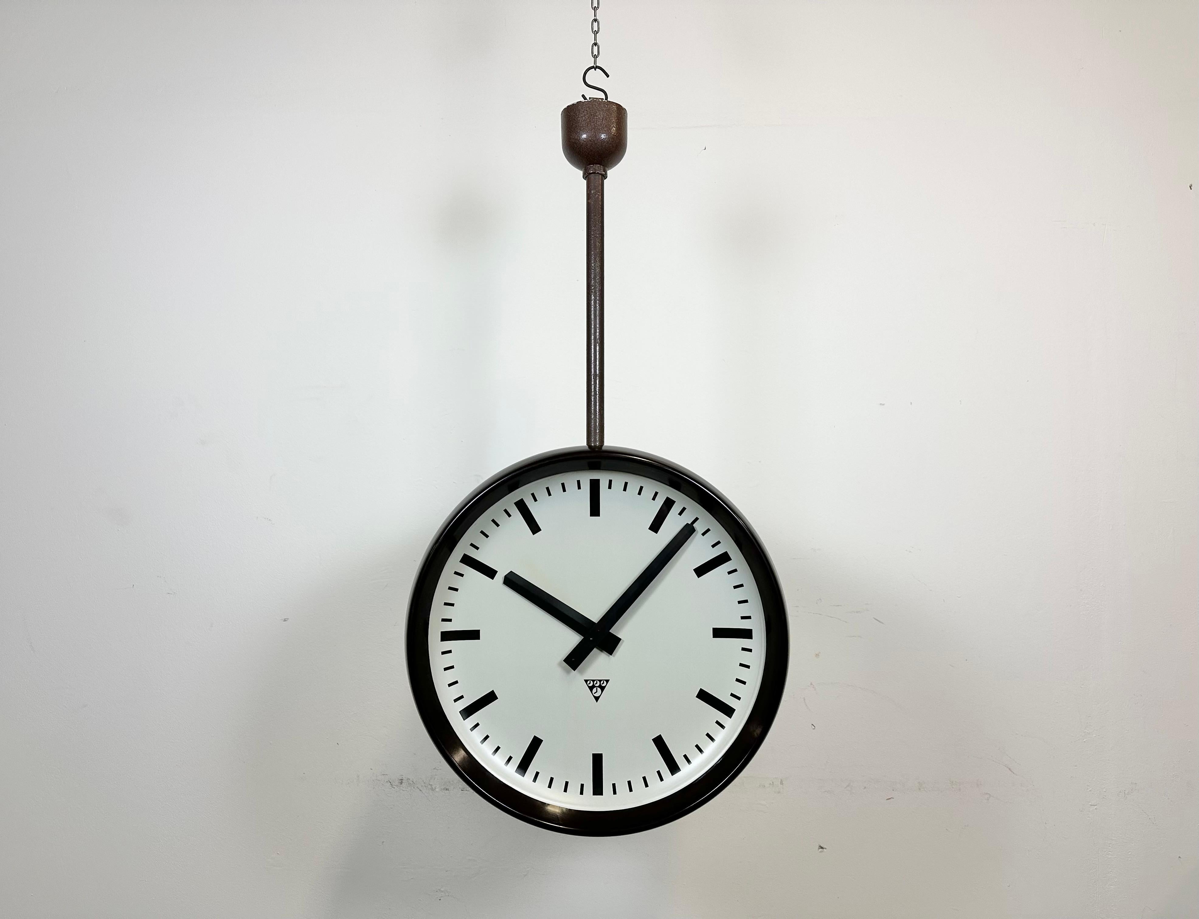 This large double-sided factory clock was produced by Pragotron, in former Czechoslovakia, during the 1950s. The piece features a two brown bakelite clock with glass cover and iron contruction. Former slave clock has been converted into a