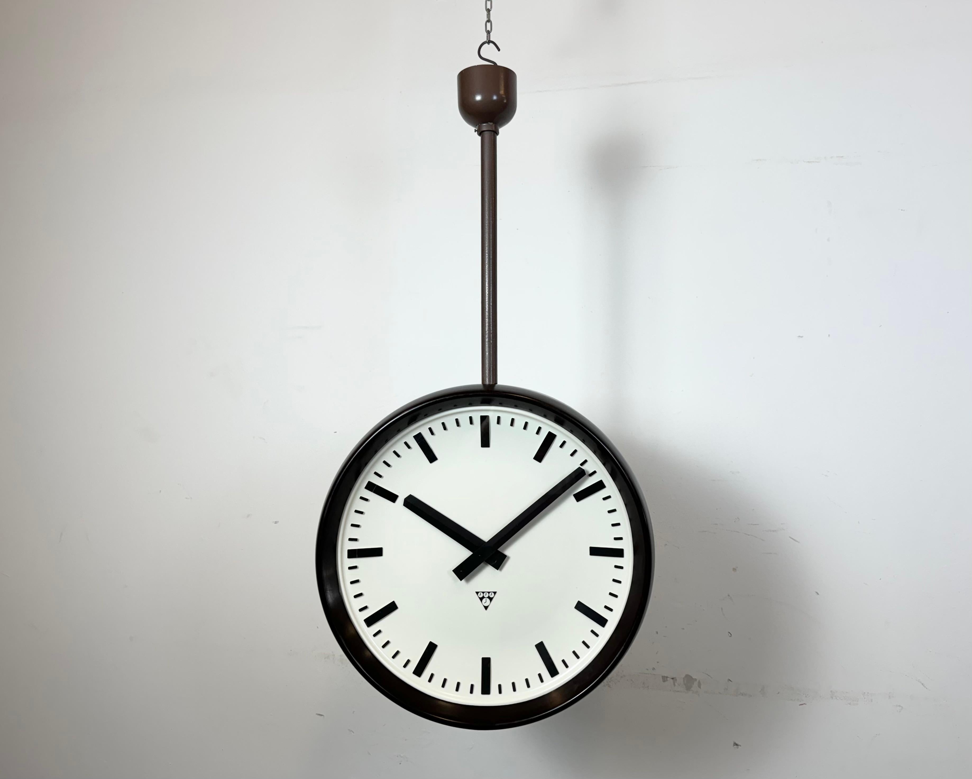 Este gran reloj de fábrica de doble cara fue producido por Pragotron, en la antigua Checoslovaquia, durante la década de 1950. La pieza presenta un reloj de baquelita marrón con tapa de cristal y estructura de hierro. El antiguo reloj esclavo se ha
