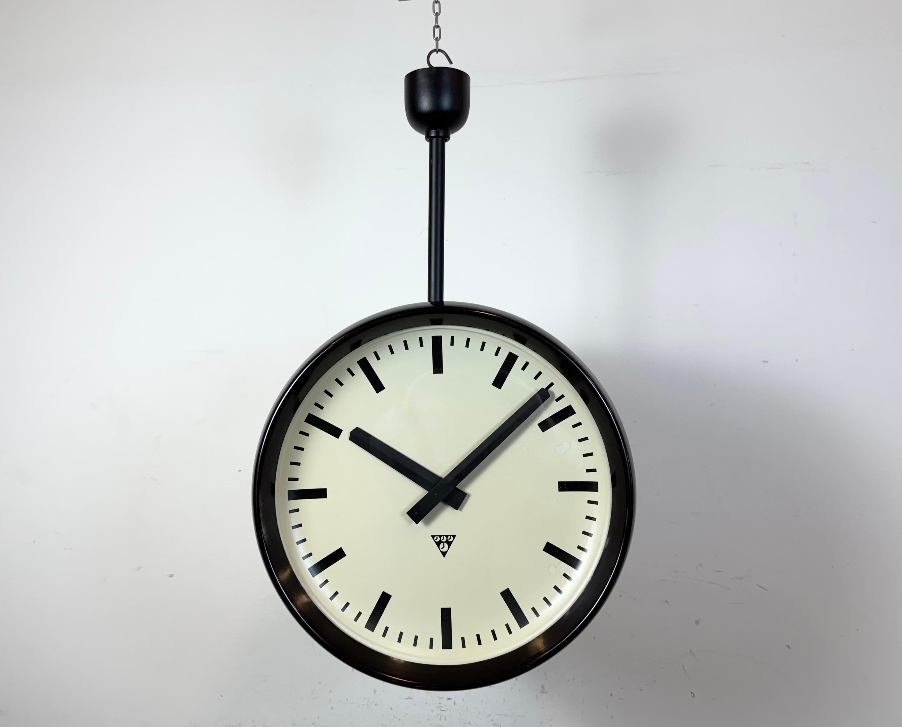 Questo grande orologio di fabbrica a doppia faccia è stato prodotto da Pragotron nell'ex Cecoslovacchia durante gli anni '50. Il pezzo presenta due cornici in bachelite marrone, quadranti in alluminio, coperture in vetro trasparente e una struttura