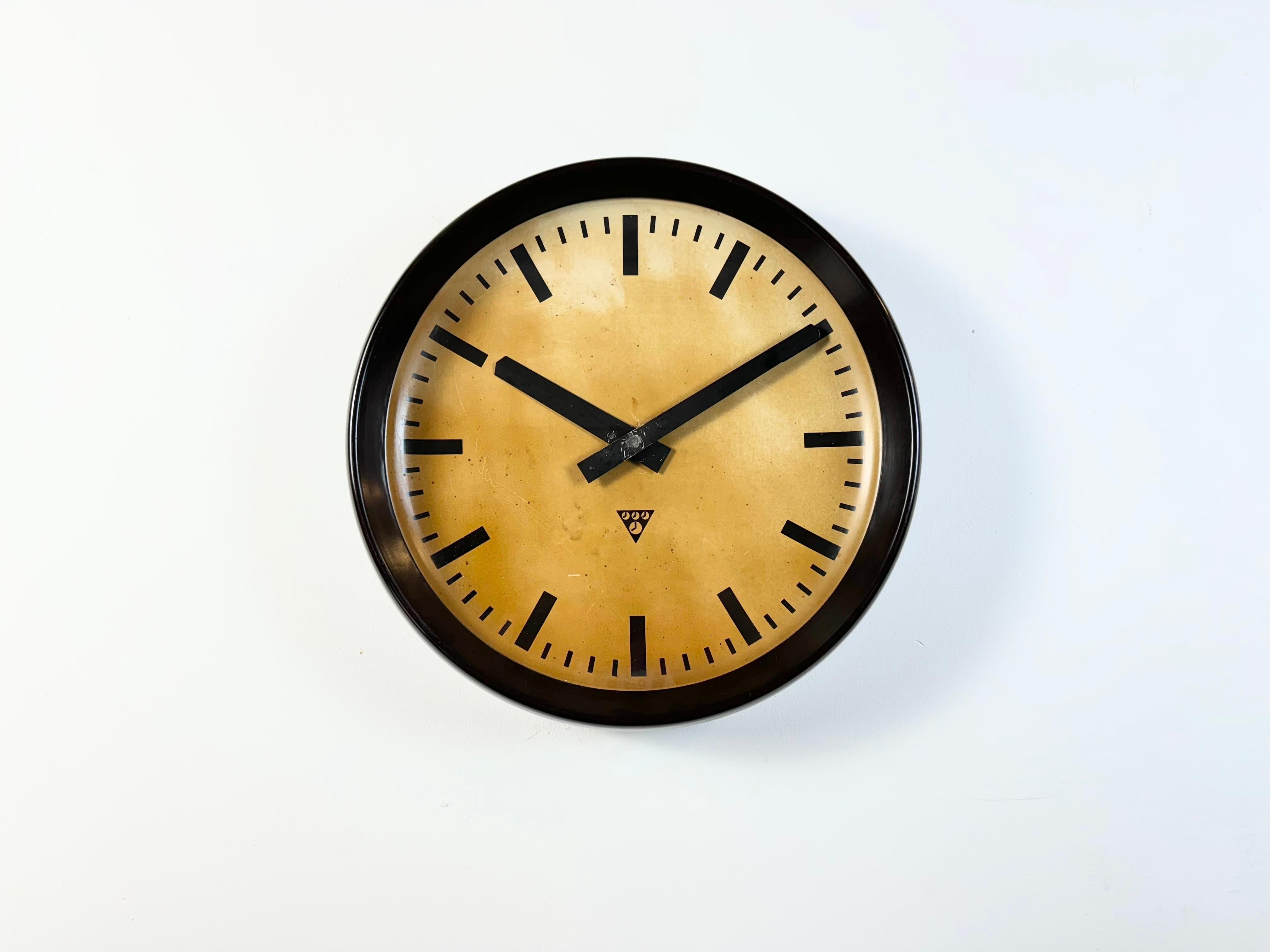 This large wall clock was produced by Pragotron in former Czechoslovakia during the 1950s. It features a brown bakelite frame, an aluminium dial and hands and a clear glass cover. The piece has been converted into a battery-powered clockwork and