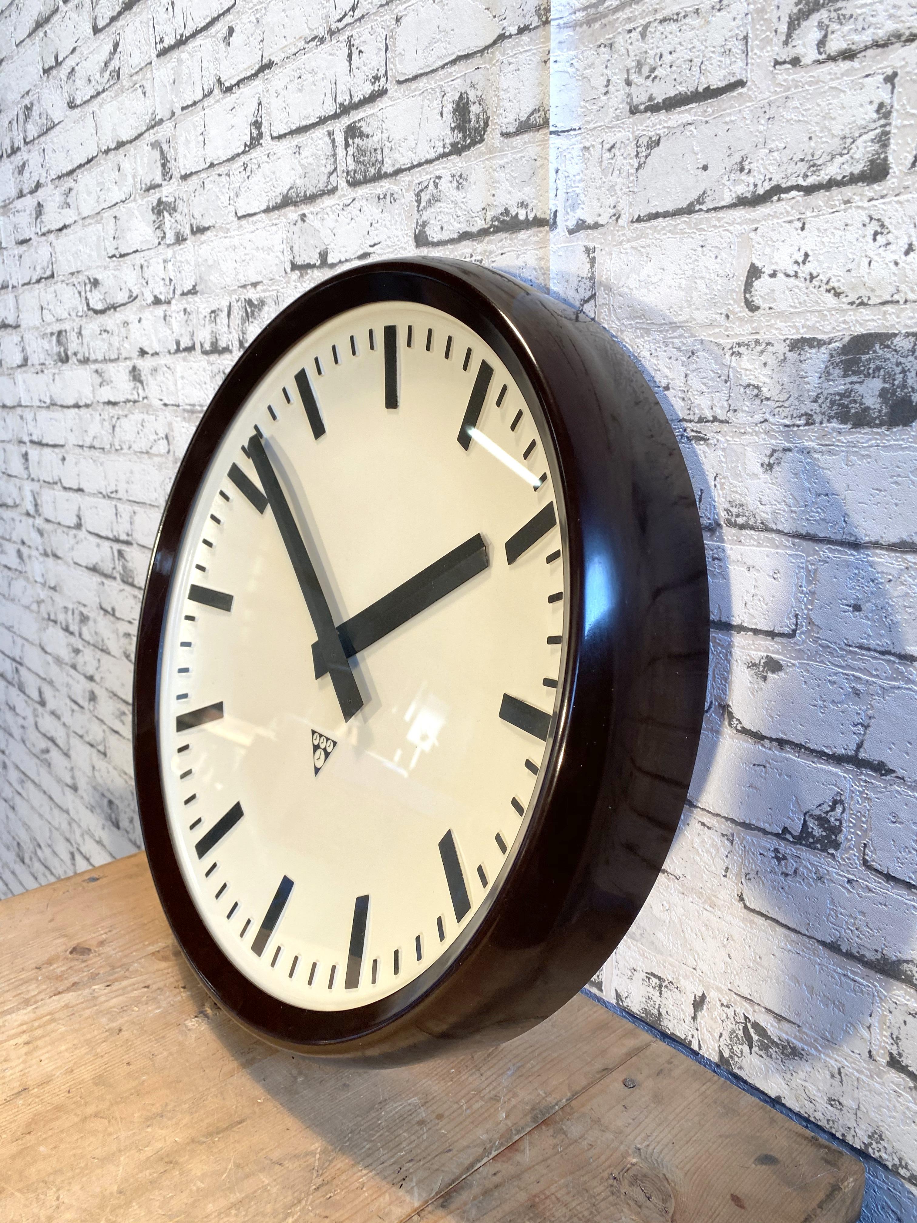 This large wall clock was produced by Pragotron in former Czechoslovakia during the 1960s.It features a brown bakelite frame, a white plastic dial, an aluminium hands and a clear glass cover. The piece has been converted into a battery-powered