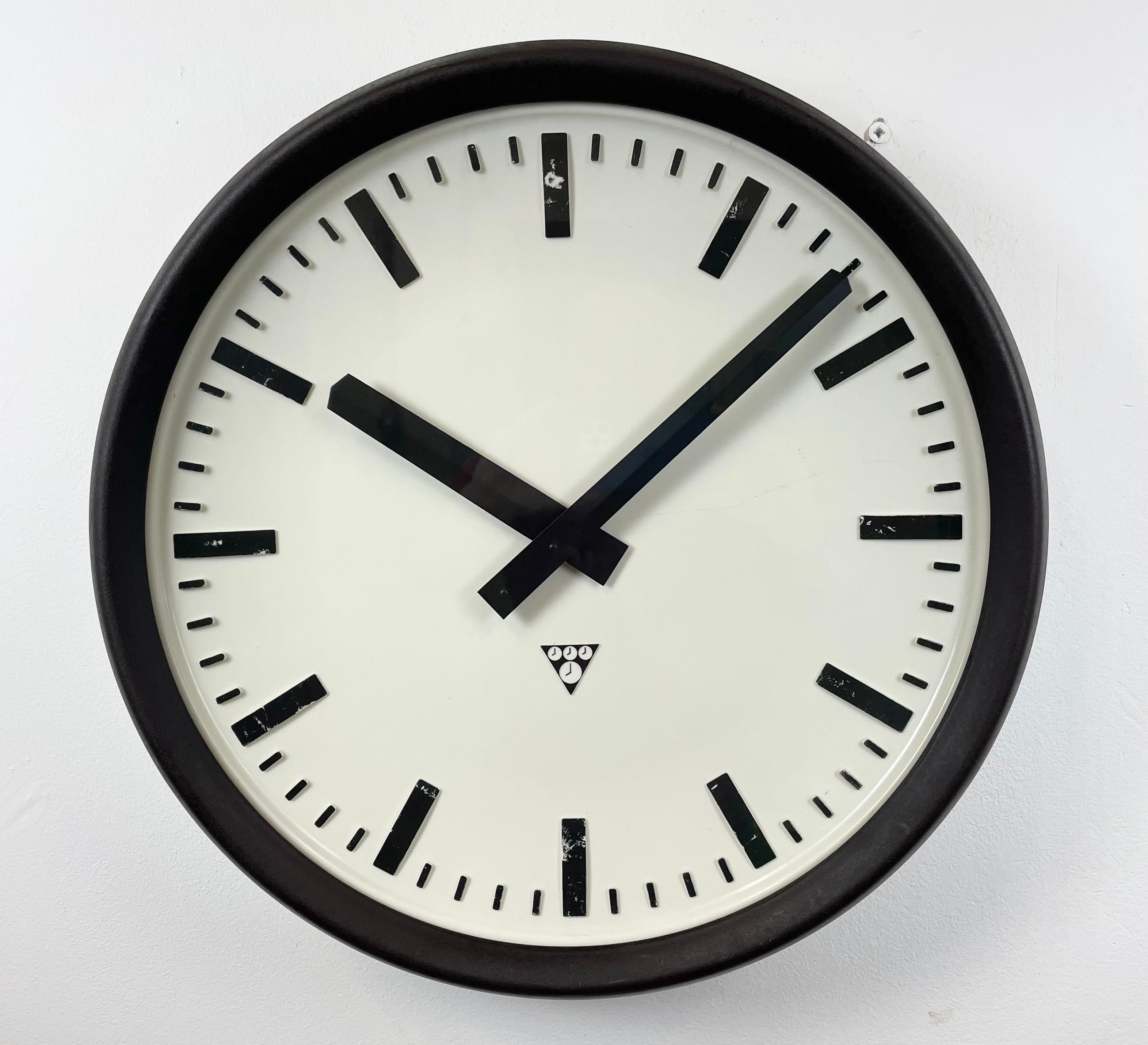 This large wall clock was produced by Pragotron in former Czechoslovakia during the 1960s. It features a brown bakelite frame, a white bakelite dial, an aluminium hands and a clear glass cover. The piece has been converted into a battery-powered