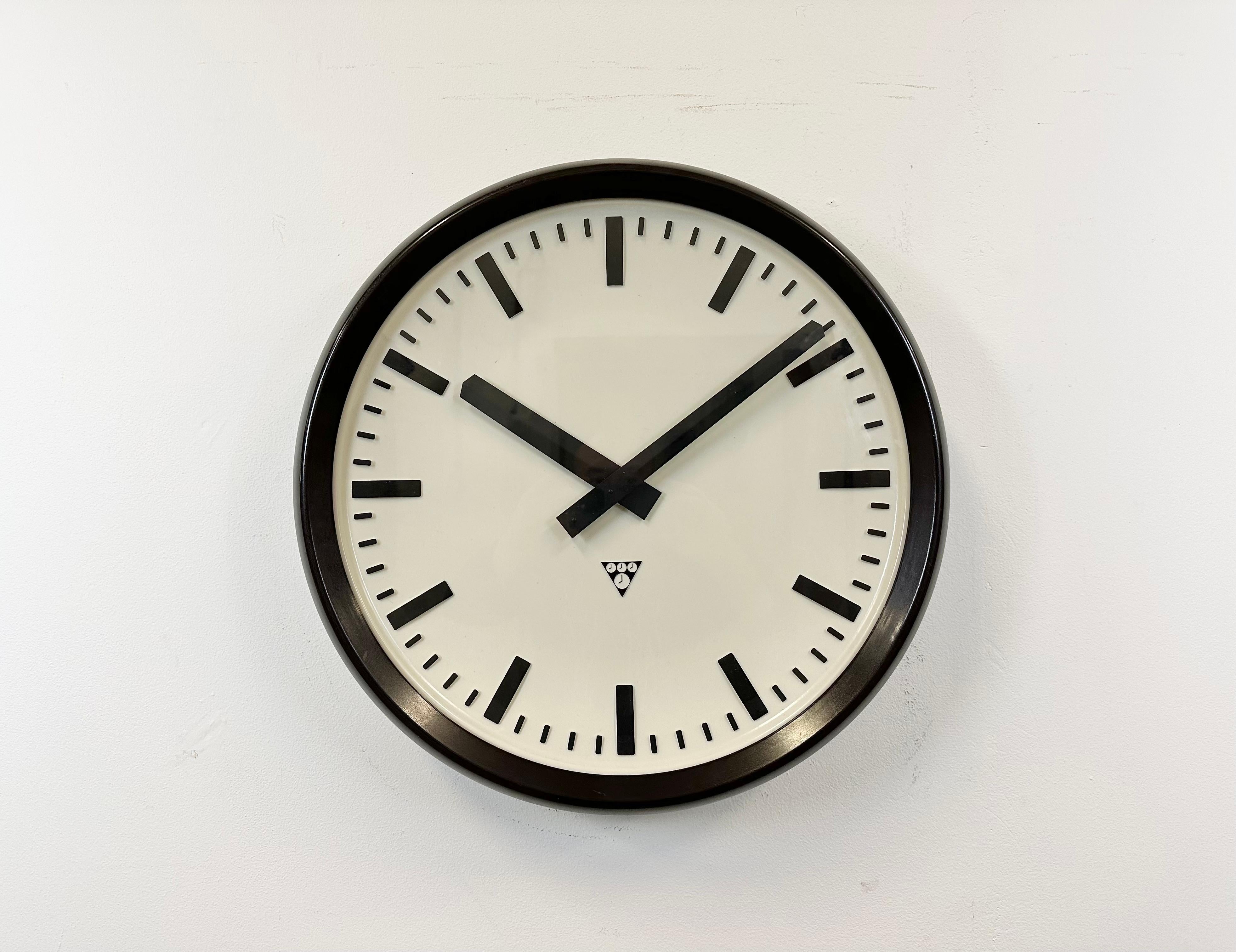 This large wall clock was produced by Pragotron in former Czechoslovakia during the 1960s. It features a brown bakelite frame, a plastic dial, an aluminium hands and a clear glass cover. The piece has been converted into a battery-powered clockwork