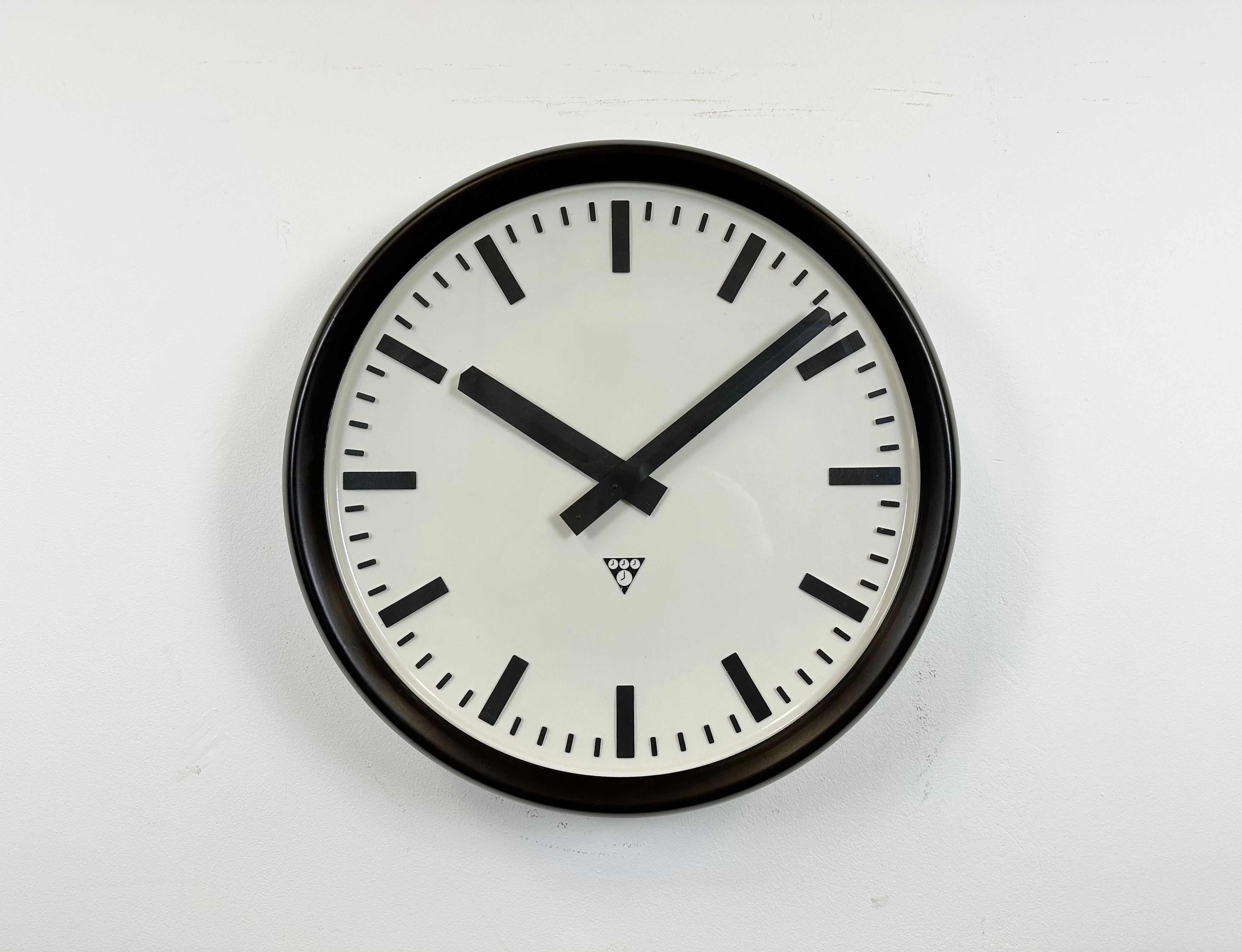 This large wall clock was produced by Pragotron in former Czechoslovakia during the 1960s. It features a brown bakelite frame and back, a plastic dial, an aluminium hands and a clear glass cover. The piece has been converted into a battery-powered