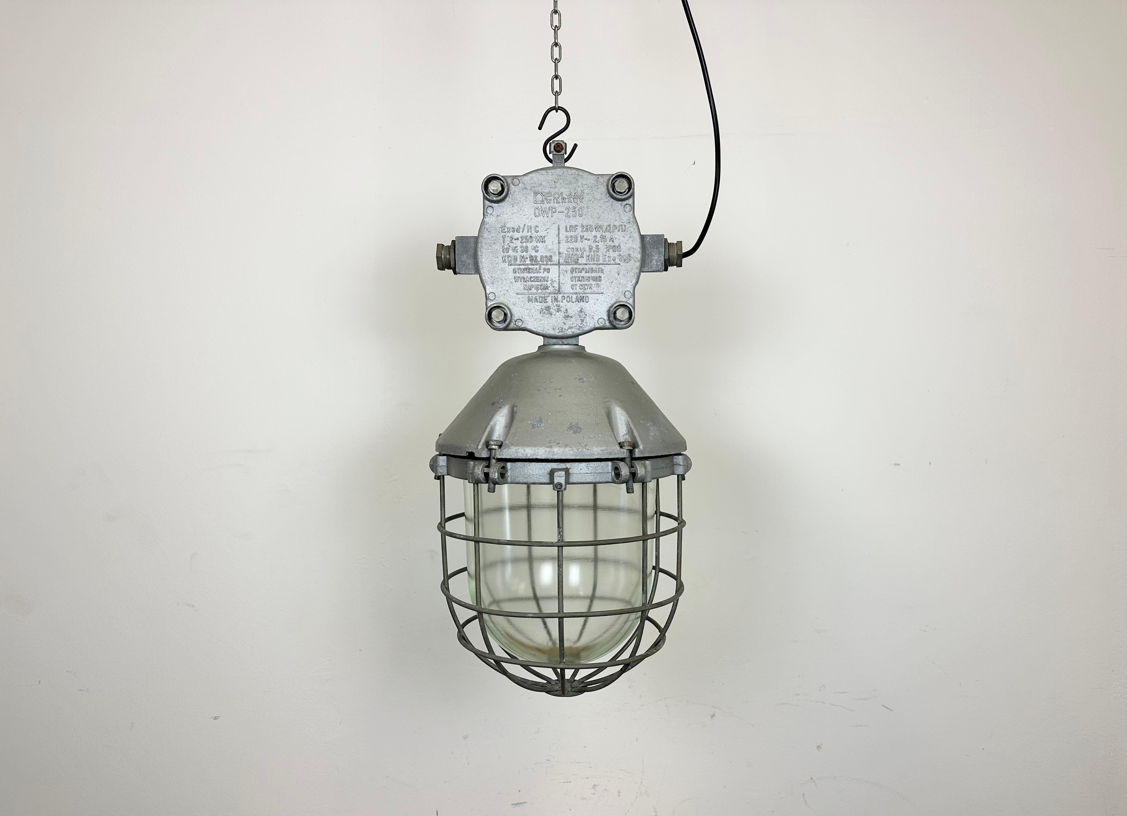 Large industrial factory hanging lamp made by Polam Wilkasy in Poland during the 1970s. It features a cast aluminium body, a clear glass cover and iron grid. The porcelain socket requires E 27/ E26 lightbulbs. New wire. The weight of the lamp is 9