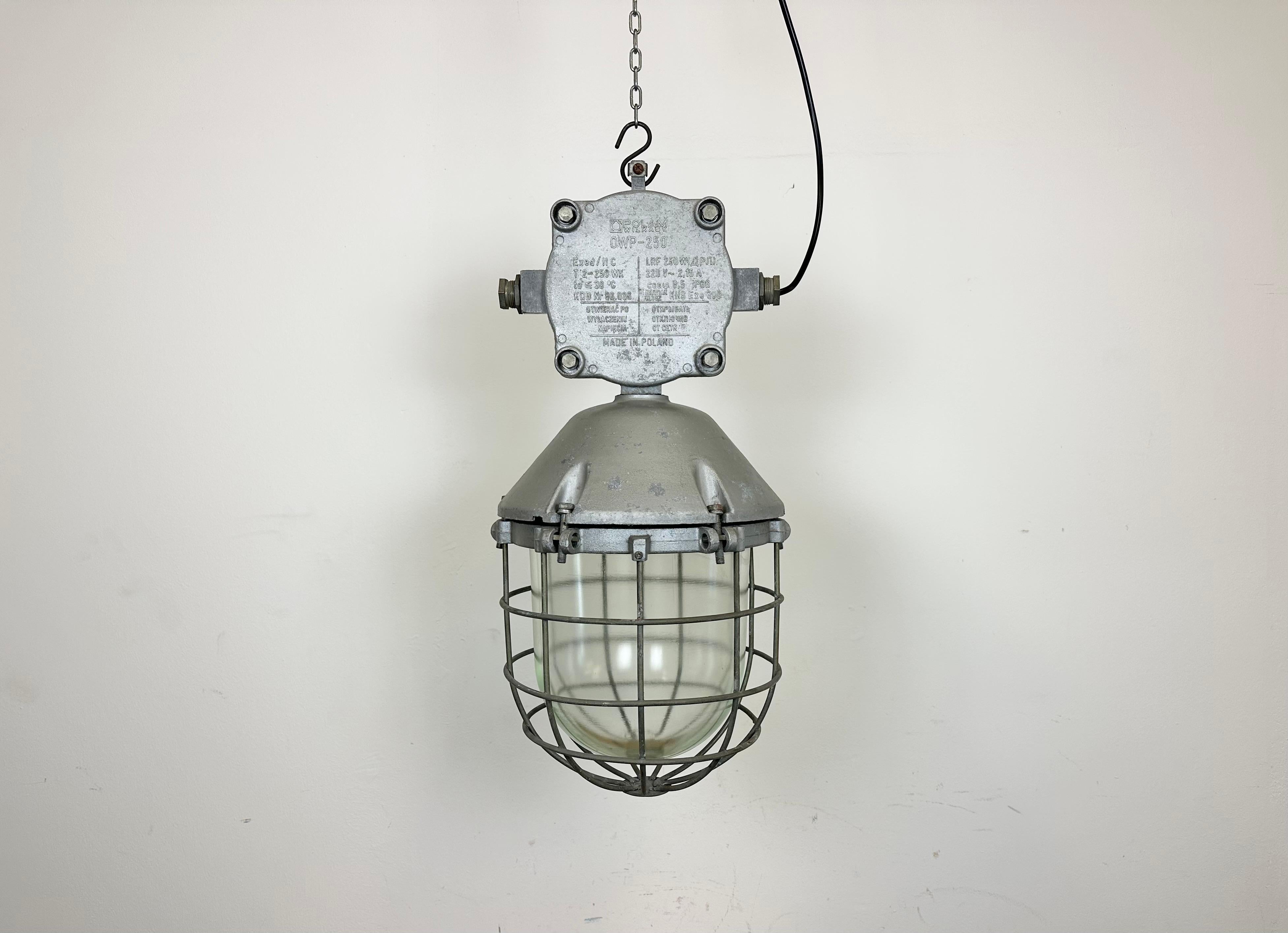 Grande lampada a sospensione industriale realizzata da Polam Wilkasy in Polonia negli anni '1970. Presenta un corpo in alluminio fuso, un coperchio in vetro trasparente e una griglia in ferro. La presa in porcellana richiede lampadine E 27/ E26. Un