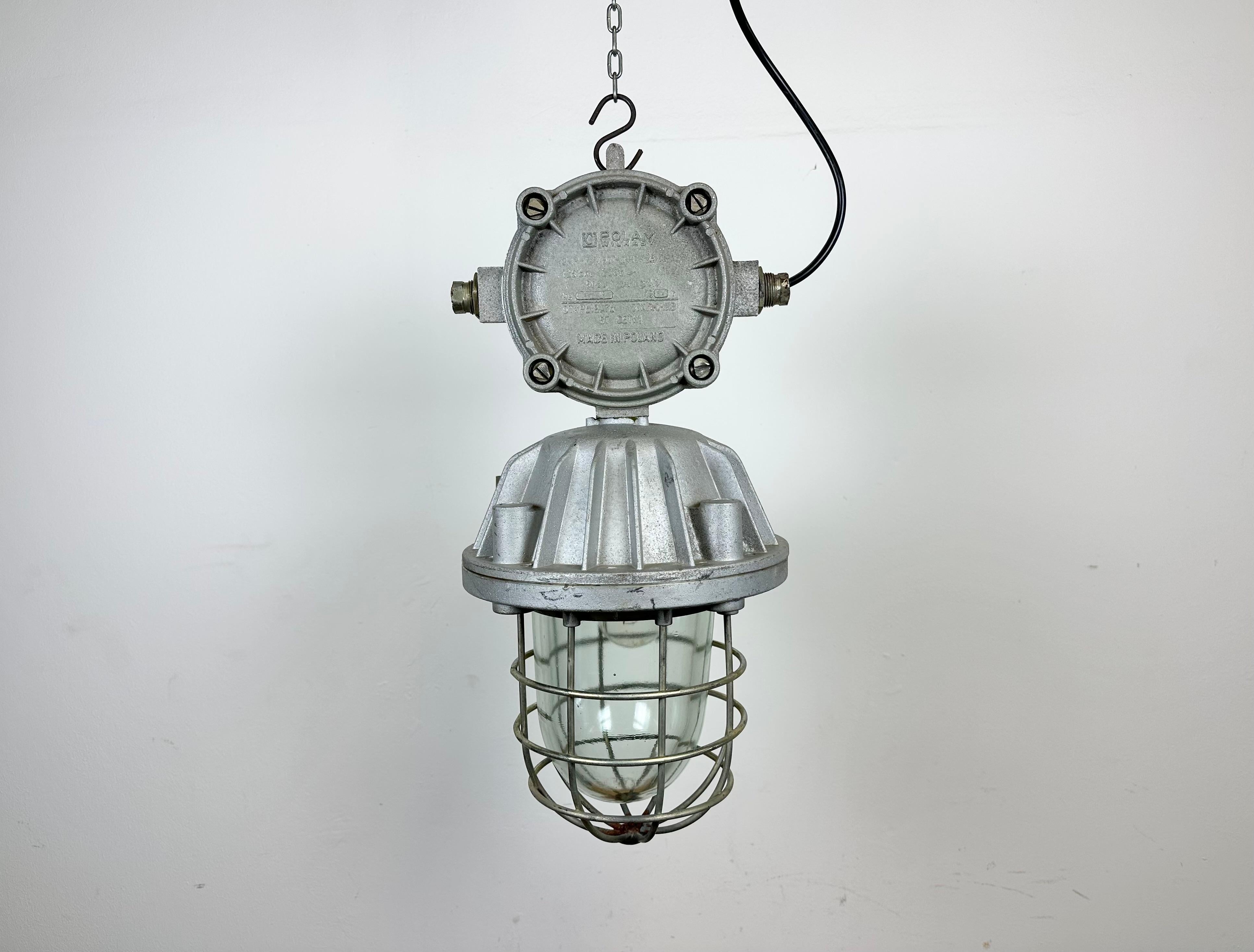 Large industrial factory hanging lamp made by Polam Wilkasy in Poland during the 1970s. It features a cast aluminium body, a clear glass cover and iron grid. The porcelain socket requires E 27/ E 26 lightbulbs. New wire. The weight of the lamp is 9
