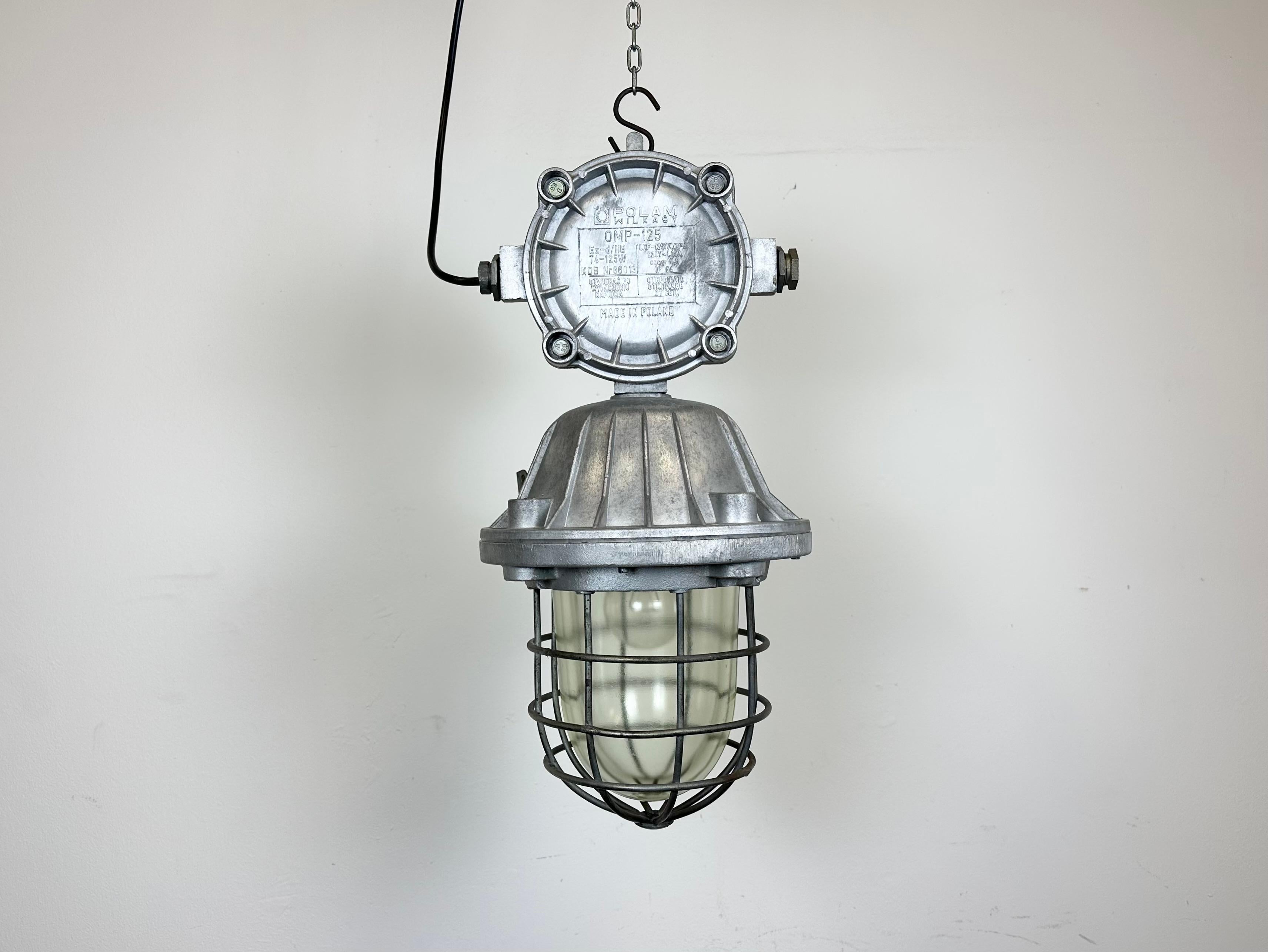 Large industrial factory hanging lamp made by Polam Wilkasy in Poland during the 1970s. It features a cast aluminium body, a clear glass cover and iron grid. The porcelain socket requires E 27/ E 26 lightbulbs. New wire. The weight of the lamp is