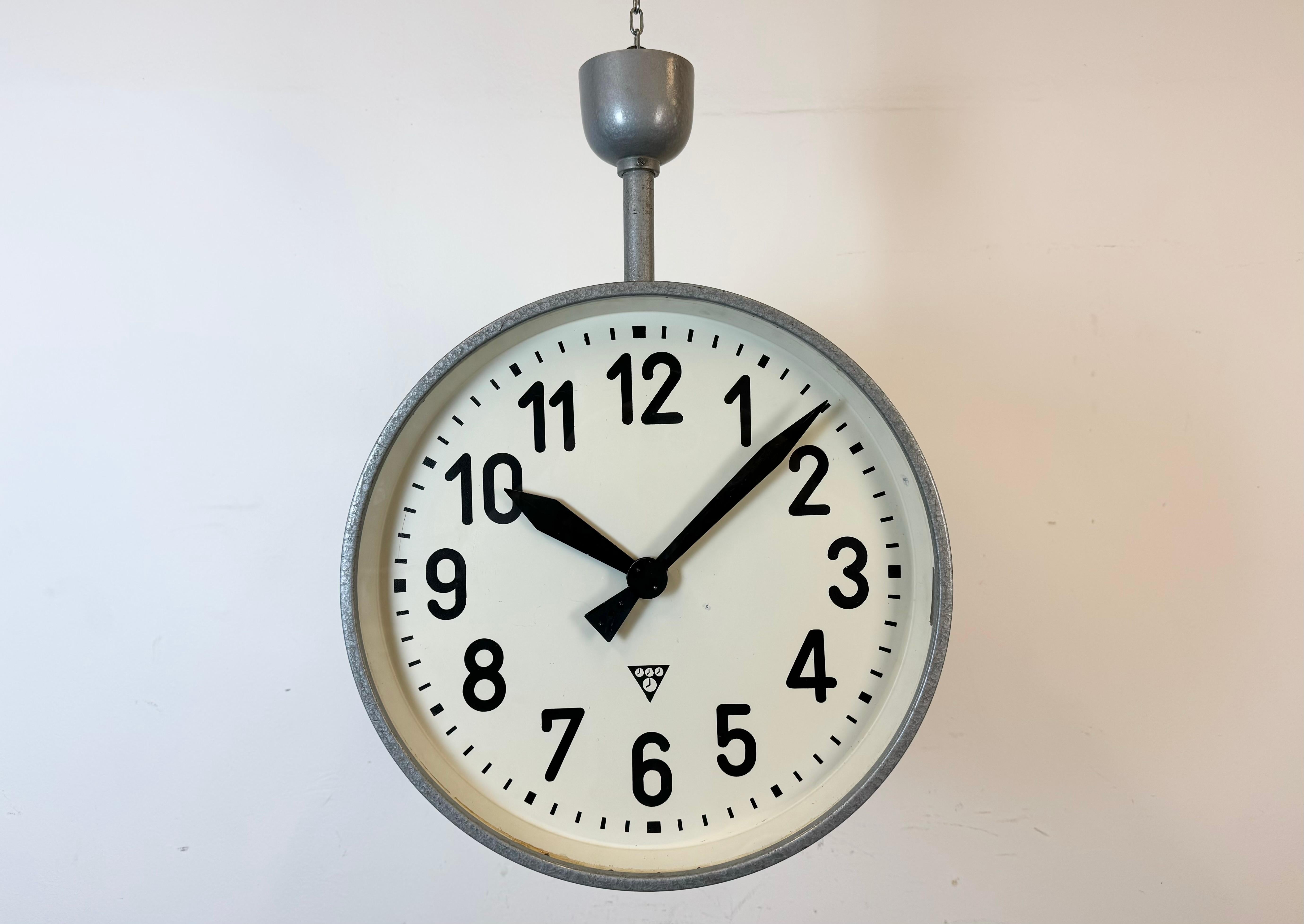 This large double sided railway or factory clock was produced by Pragotron, in former Czechoslovakia, during the 1950s. The piece features a grey hammer paint metal body and a clear glass cover. The clock has been converted into a battery-powered