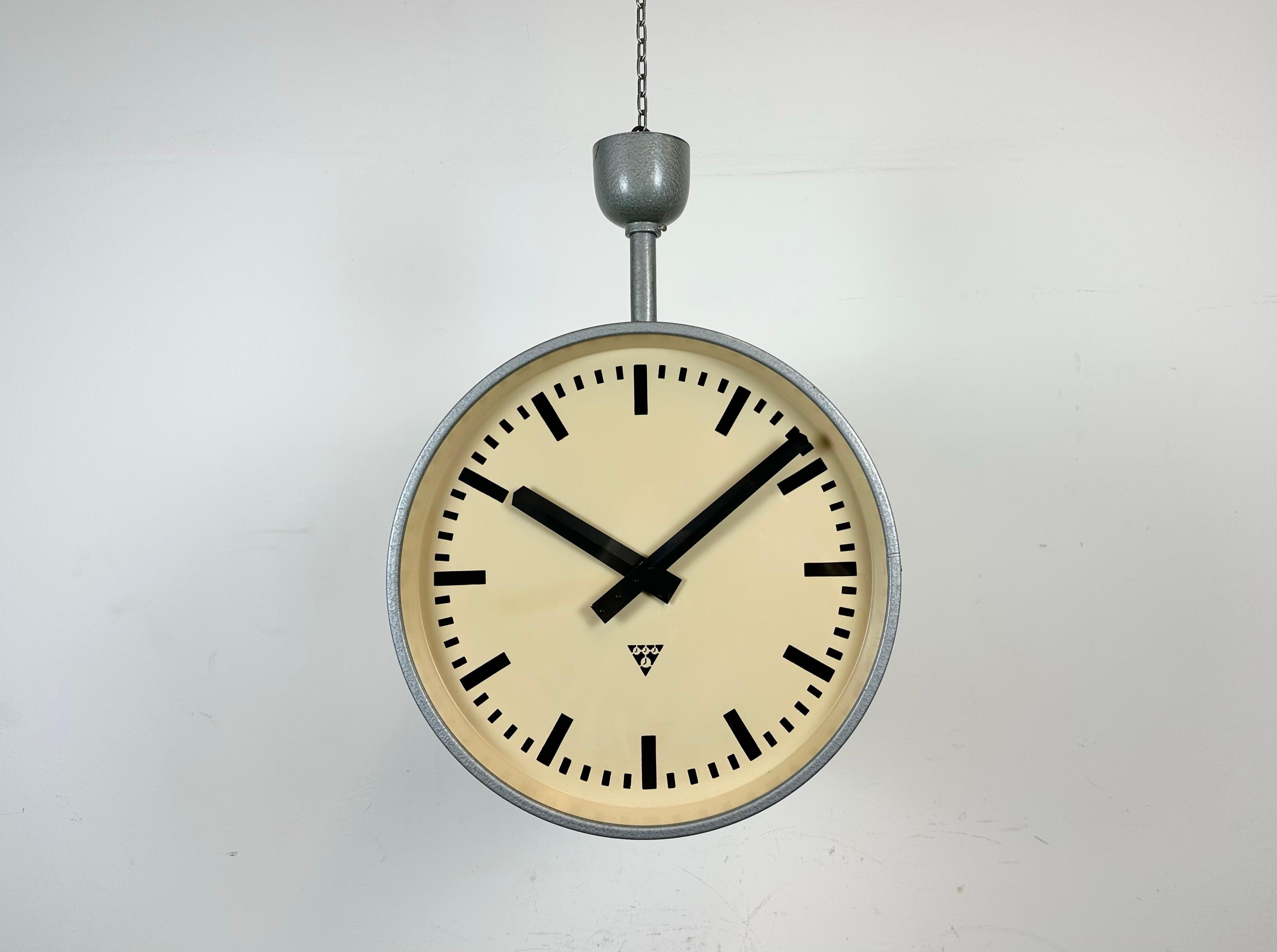 This large double sided railway or factory clock was produced by Pragotron, in former Czechoslovakia, during the 1960s. The piece features a grey hammer paint metal body and a clear glass cover. The clock has been converted into a battery-powered