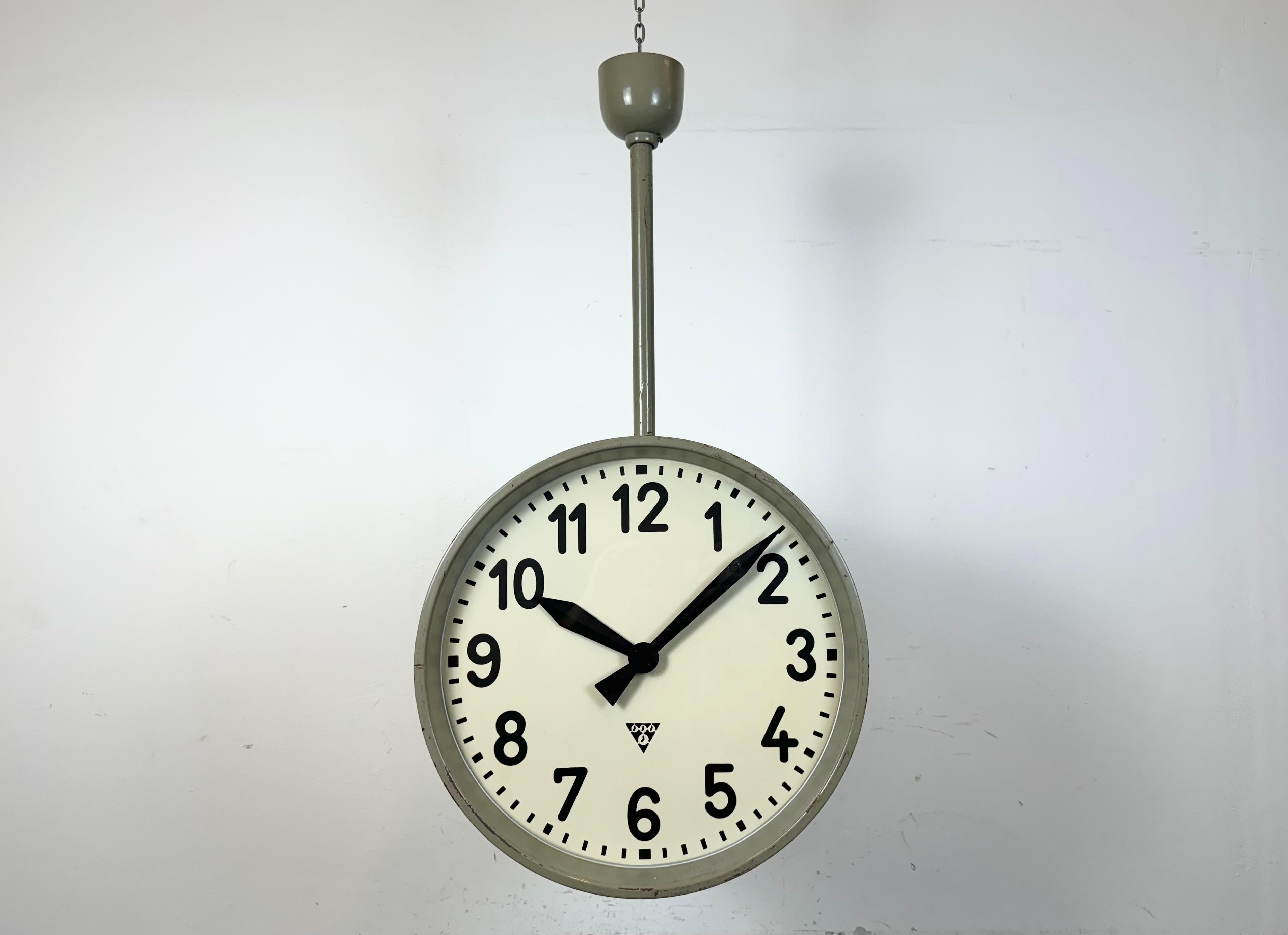 This large double sided railway or factory clock was produced by Pragotron, in former Czechoslovakia during the 1960s. The piece features a grey metal body and a clear glass cover. The clock has been converted into a battery-powered clockworks and