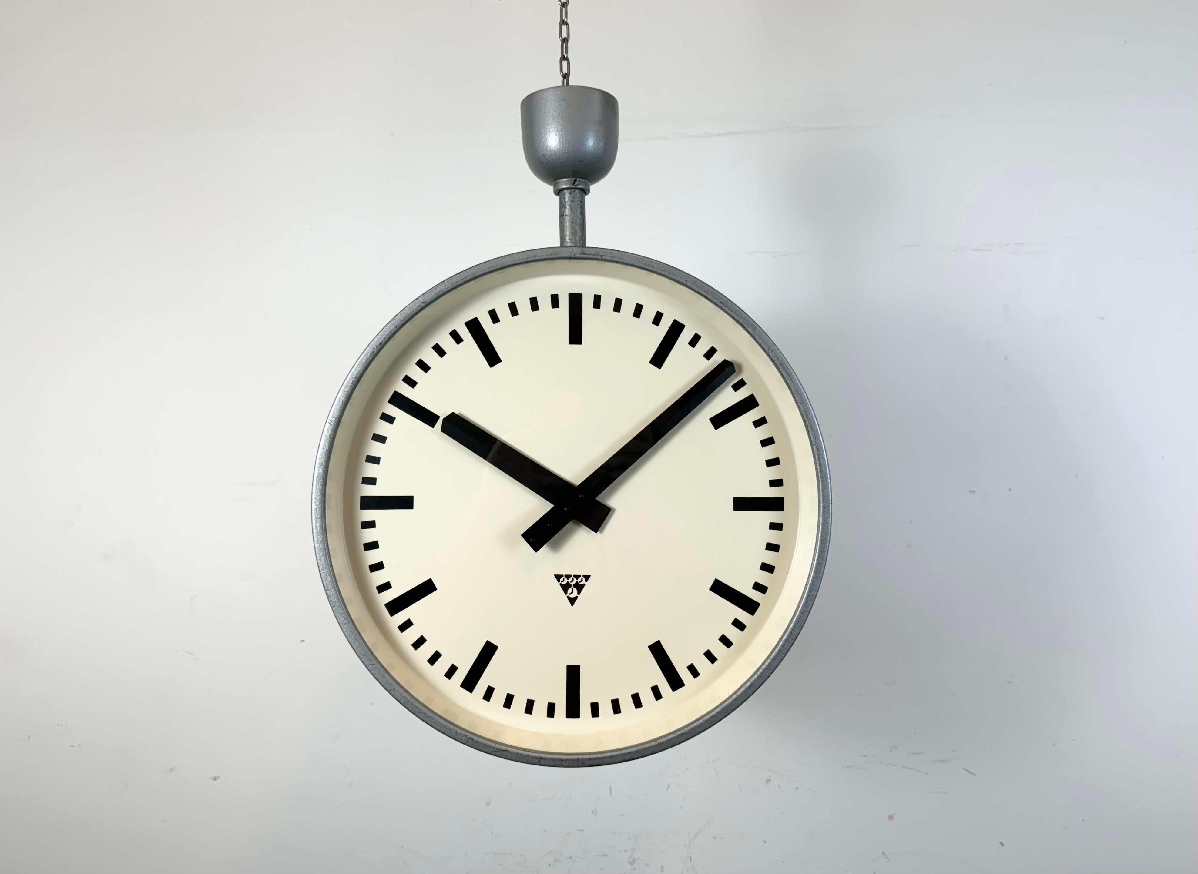 This large double sided railway or factory clock was produced by Pragotron, in former Czechoslovakia, during the 1960s. The piece features a grey metal body and a clear glass cover. The clock has been converted into a battery-powered clockworks and