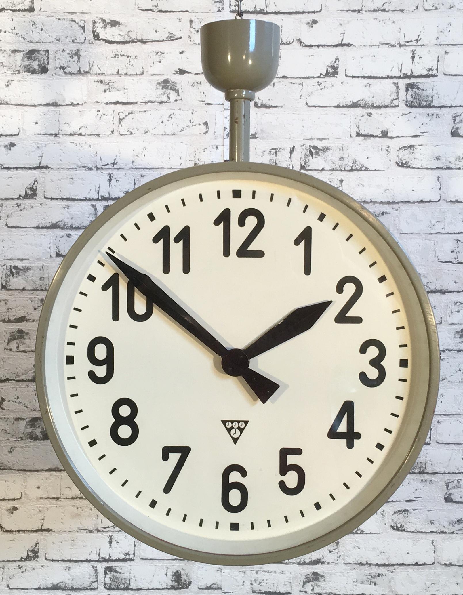 This large double-sided railway or factory clock was produced by Pragotron, in former Czechoslovakia, during the 1950s. The piece features a grey metal body and a clear glass cover. The clock has been converted into battery-powered clockwork and