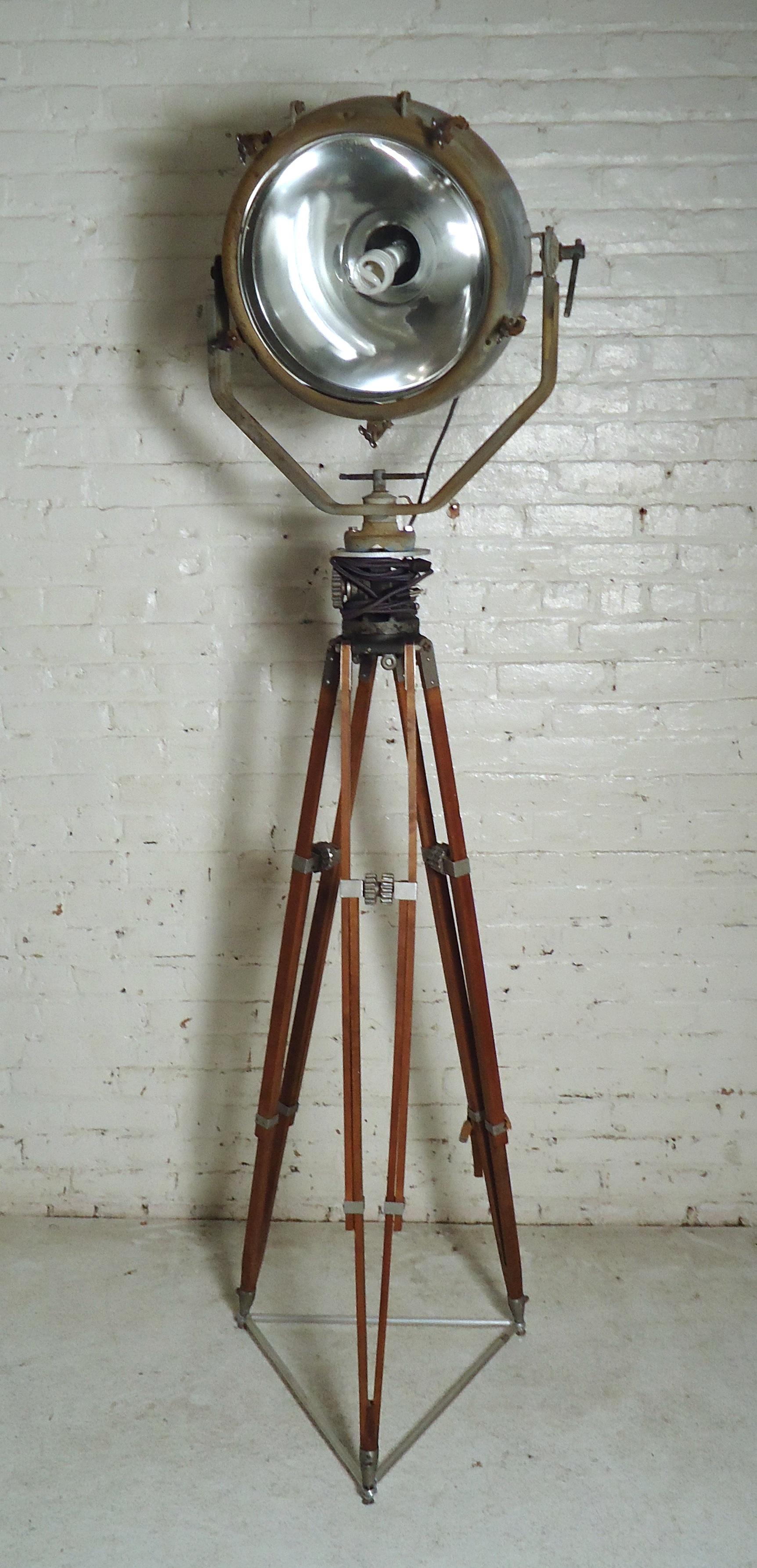 Large metal spotlight on wooden tripod base. Lamp head has metal hardware and trim, also featuring glass shield, adjustable legs, and tilting head.

(Please confirm item location - NY or NJ - with dealer)

  