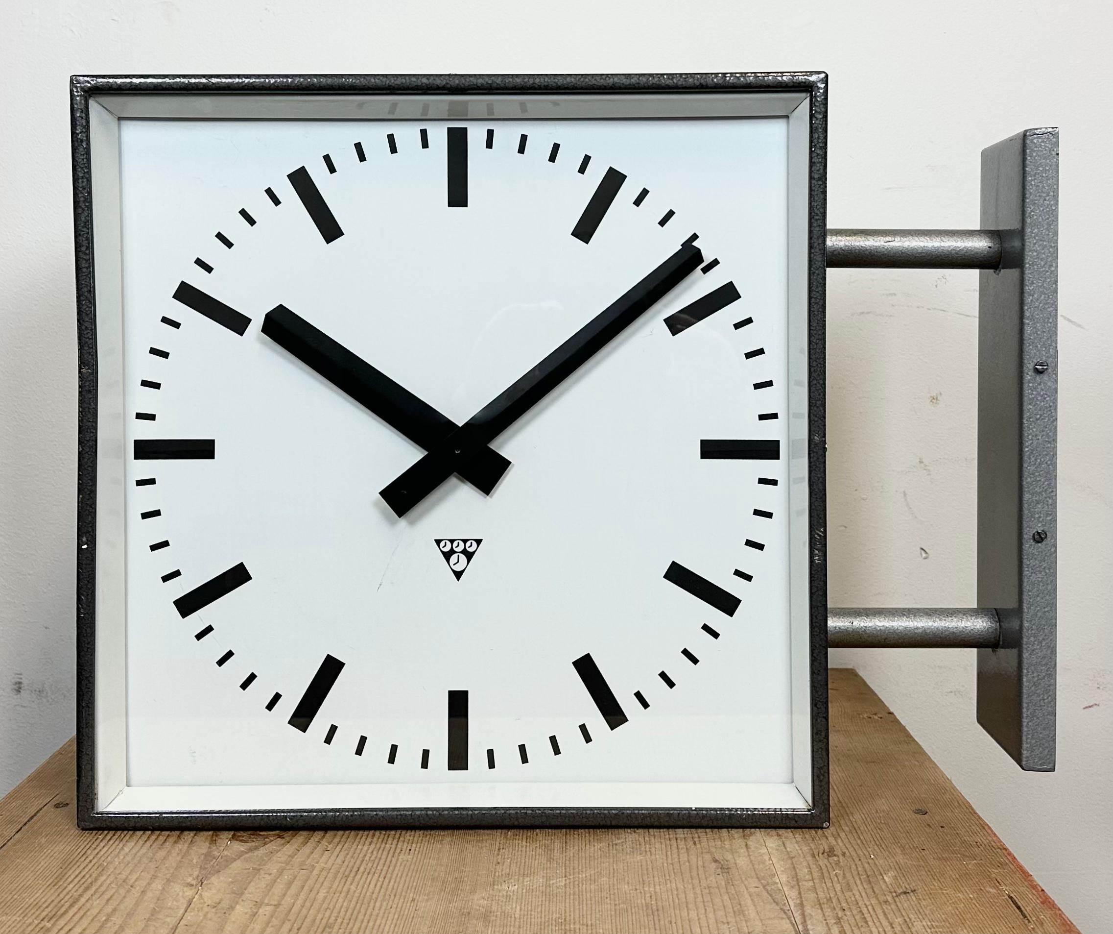 This square double sided railway, school or factory wall clock was produced by Pragotron, in former Czechoslovakia, during the 1970s. The piece features a grey metal body, a dark grey hammer paint clock frames, a clear glass covers, and an aluminum