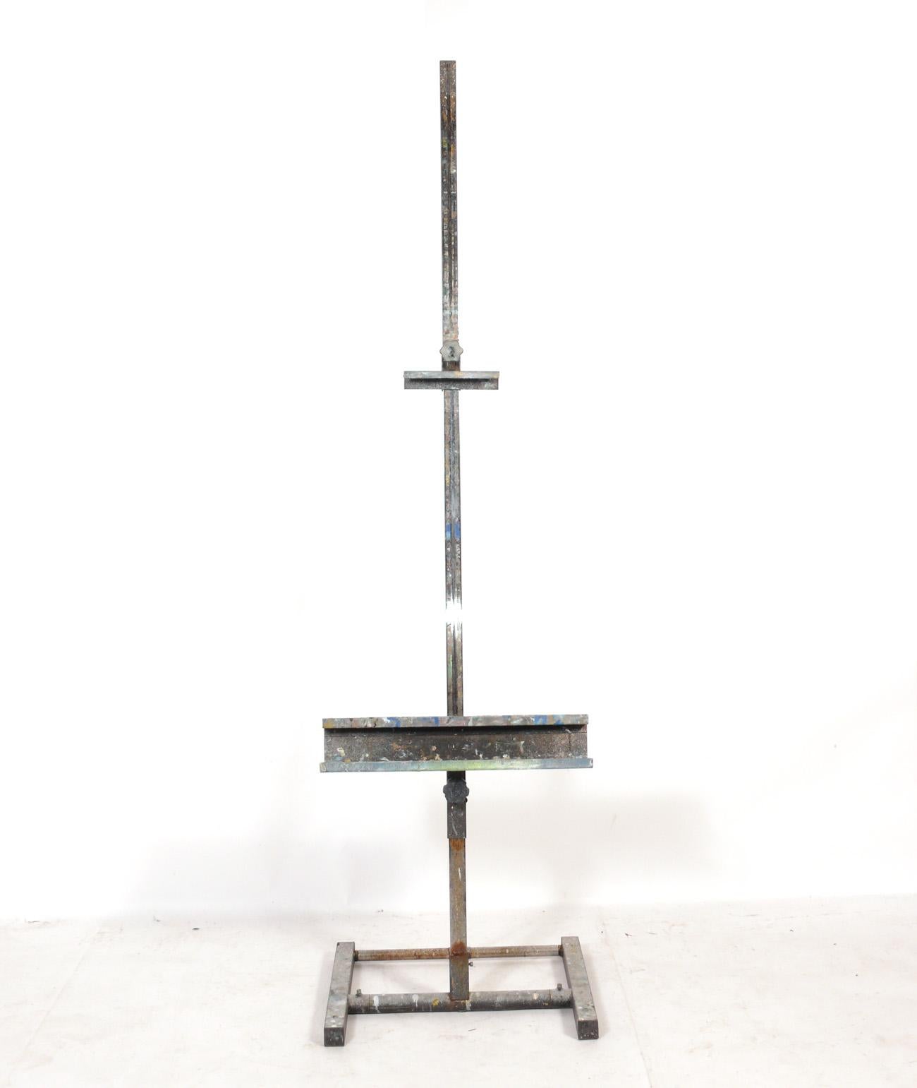 Large Industrial Style Metal Artist's Easel, American, circa 1960s. Retains it's wonderful original paint splattered patina. Would work well to hold a large painting or flat screen TV. The shelf opening when fully open is 54.75