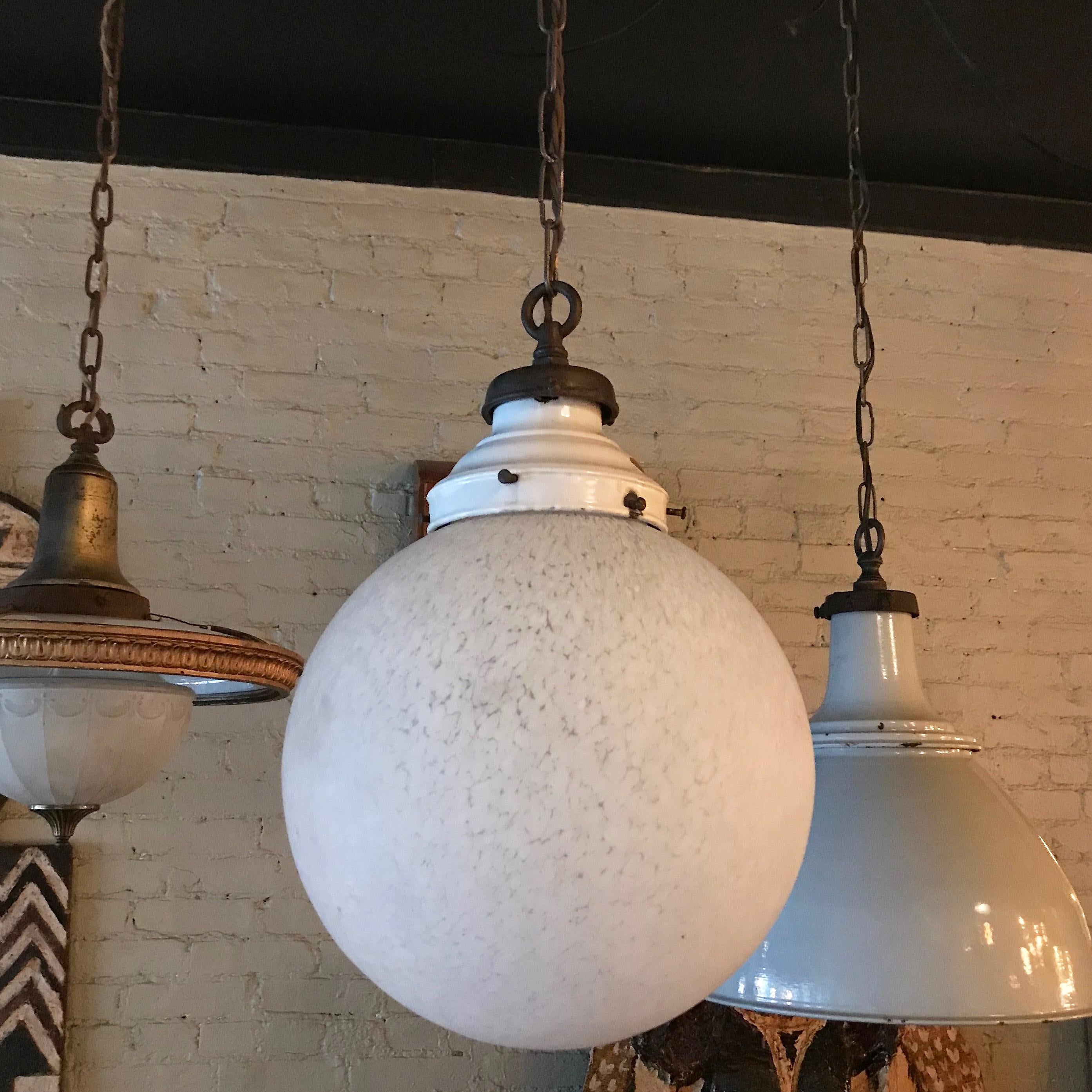 Large Industrial pendant light features a frosted glass globe shade with white enameled metal fitter on brass chain finished with brass canopy for the ceiling. The pendant is wired with braided cloth cord to accept up to a 300 watt bulb with the