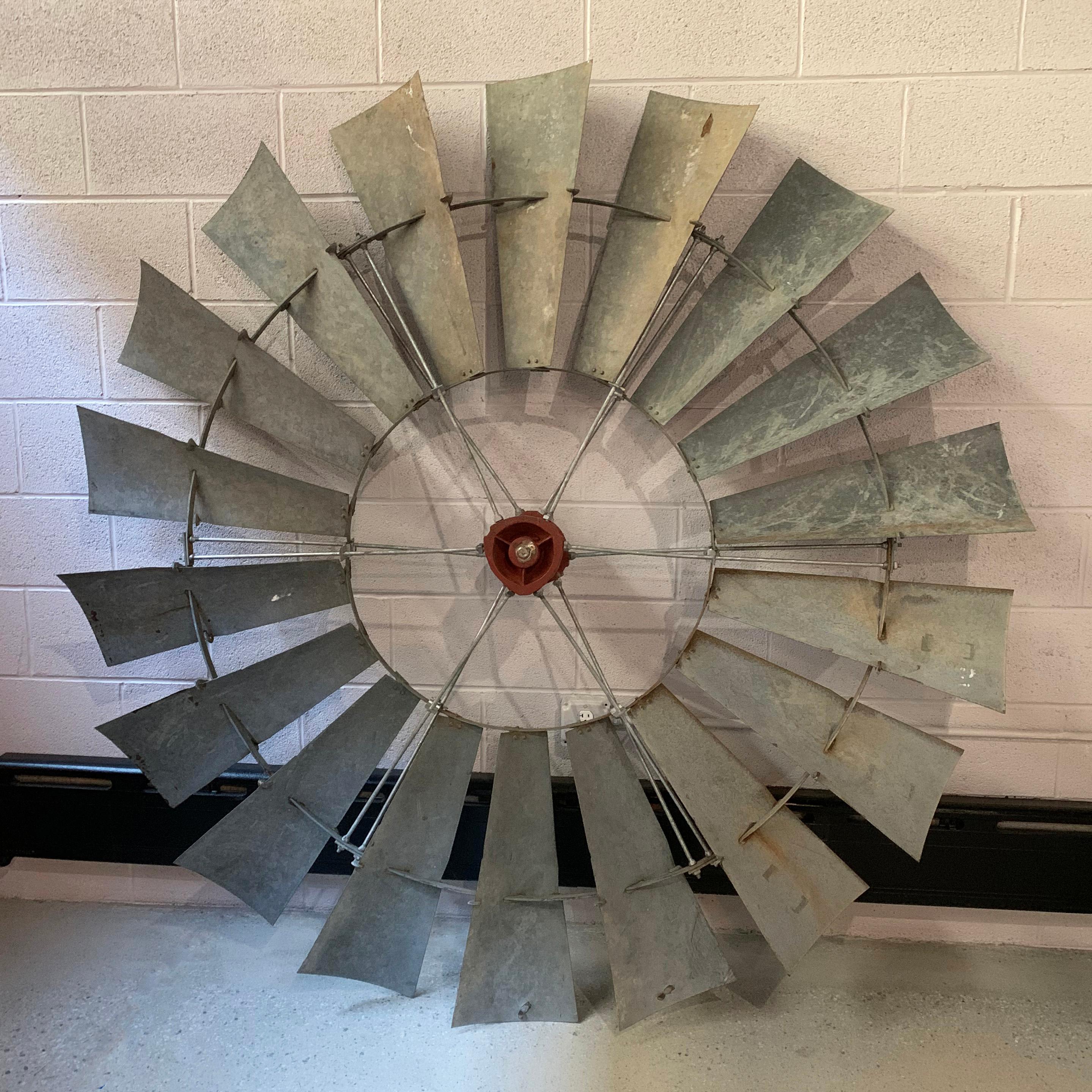 Large, 6 foot diameter, industrial, architectural, windmill wheel features galvanized sheet metal blades that are 21.75 inches long and 9 inches wide and a red cast iron bearing housing. Perfect as a repurposed, industrial, folk art piece.