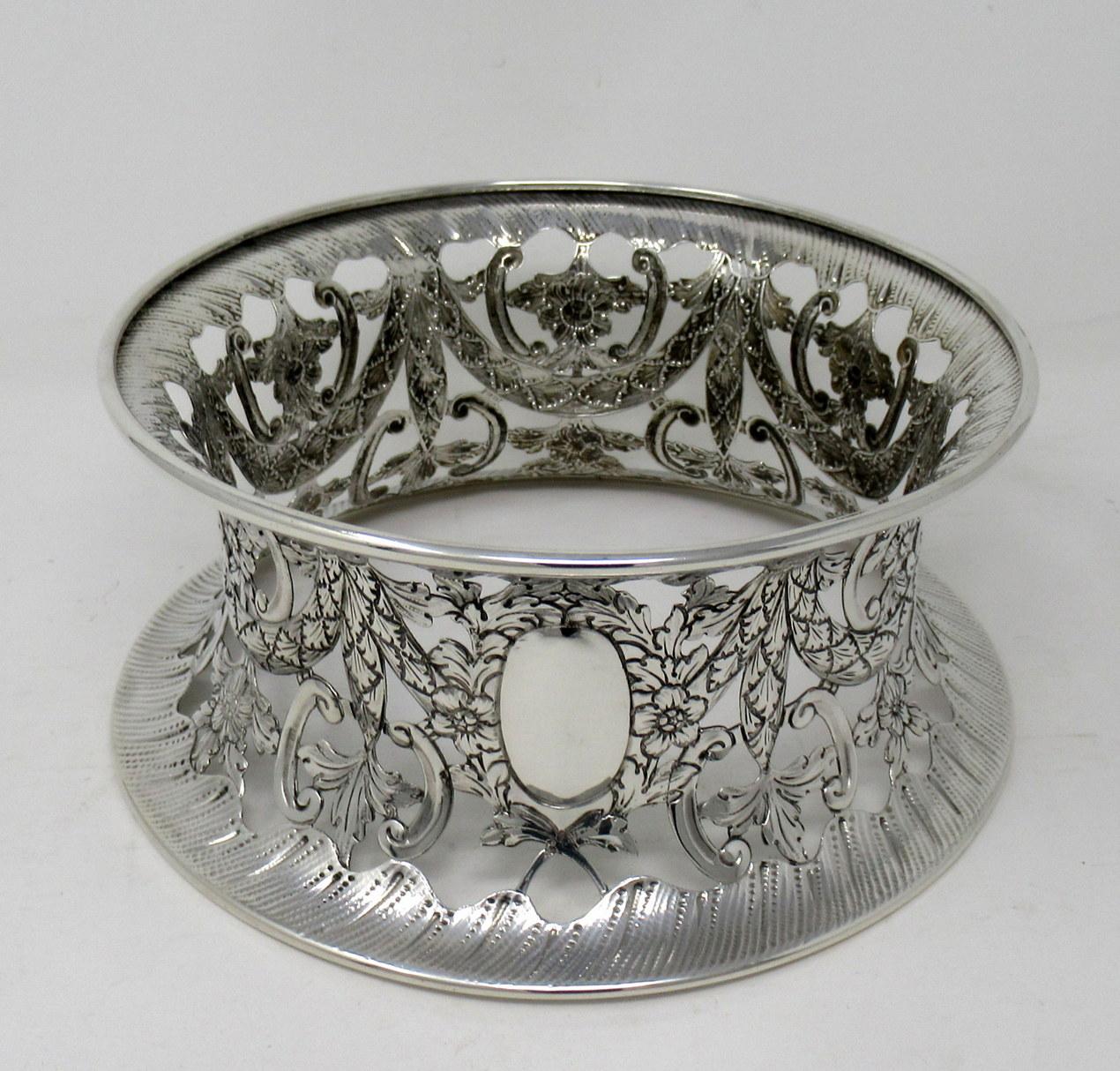 An exquisite Georgian style sterling silver English heavy Gauge table dish ring of traditional waisted form and unusually large size. 

The circular inverted sided lavish pierced body depicting chased garlands and swags with flowers. The central